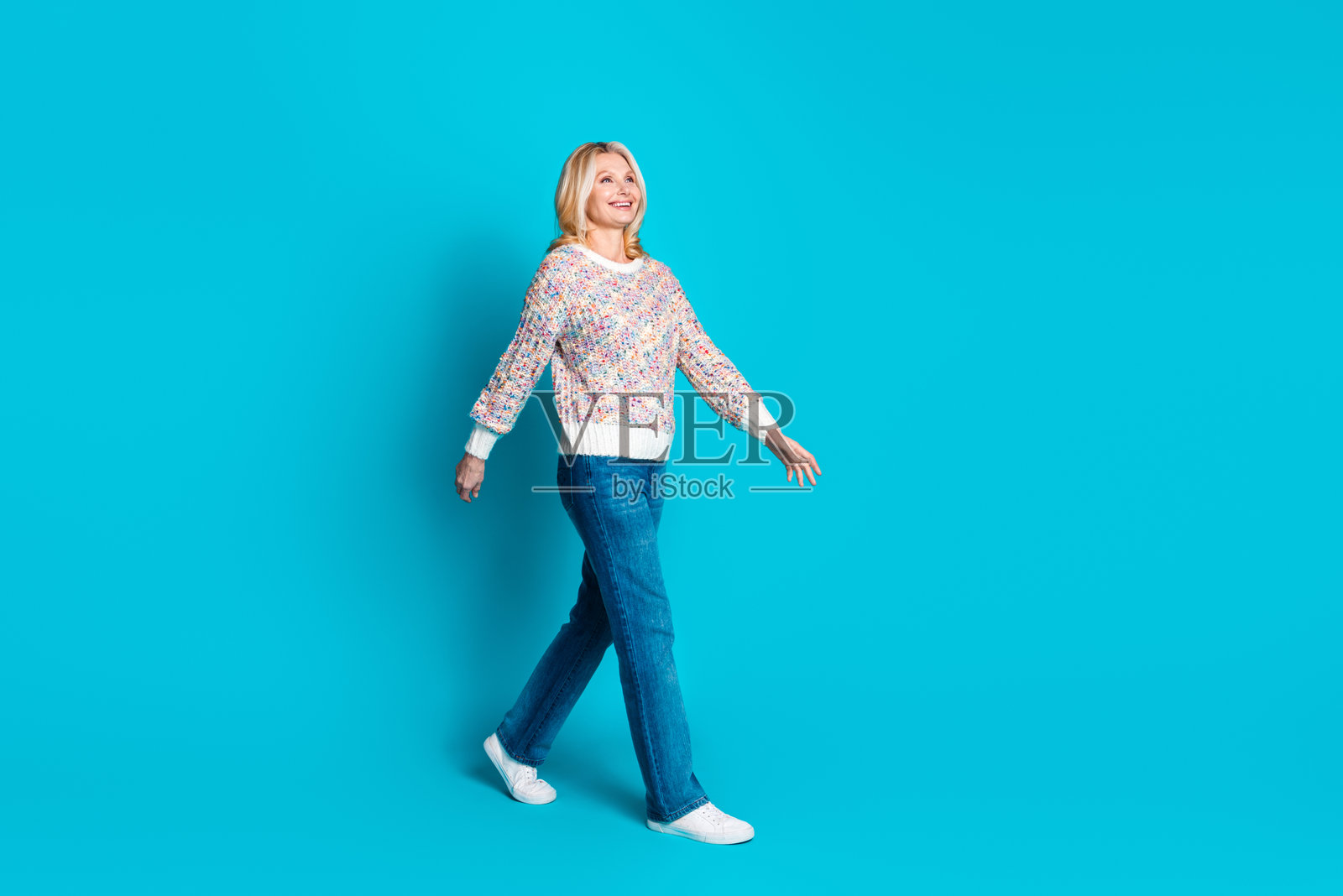 全身肖像，友好的老年女性穿着毛衣在空旷的空间中行走，背景为青绿色。照片摄影图片