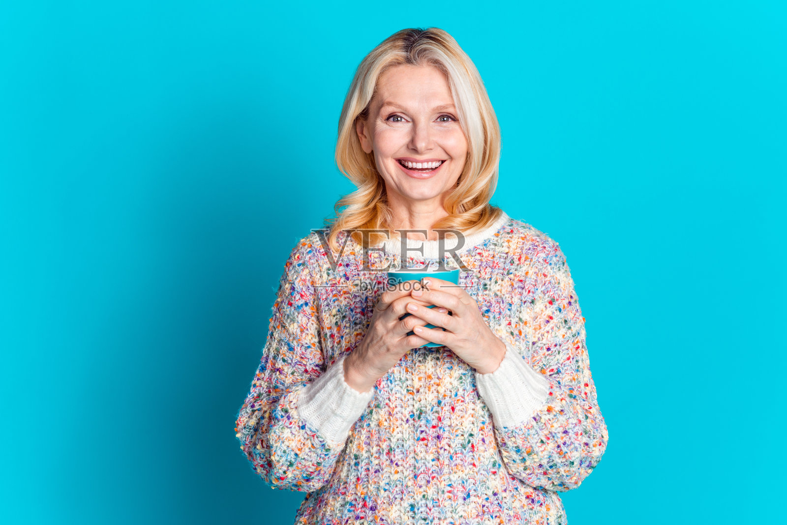 穿着毛衣的漂亮老年女士手持咖啡杯，背景为青绿色。照片摄影图片