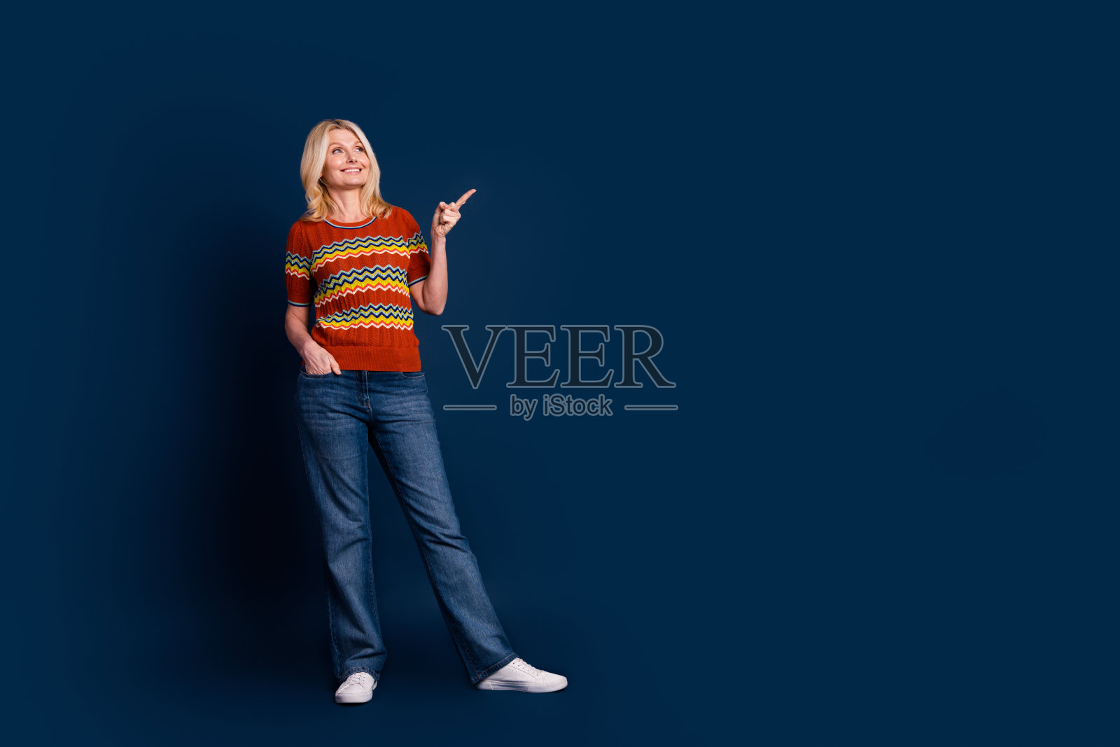 穿着条纹时尚服装的快乐可爱漂亮女性，面带微笑，凝视空旷的空间，背景为深蓝色。照片摄影图片