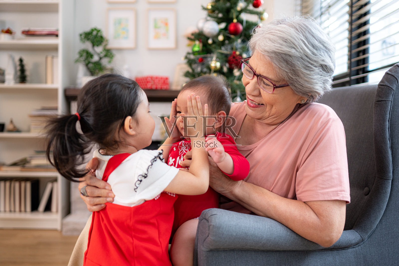 奶奶坐在扶手椅上，抱着她的婴儿孙子，愉快地和他聊天，客厅里装饰着即将到来的圣诞节的装饰。照片摄影图片