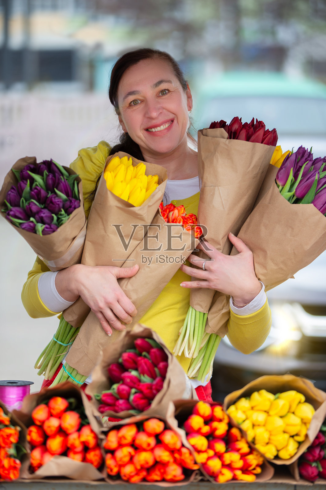 一位手捧郁金香花束的女性。市场上的花贩微笑着看向镜头，手中拿着花束。照片摄影图片