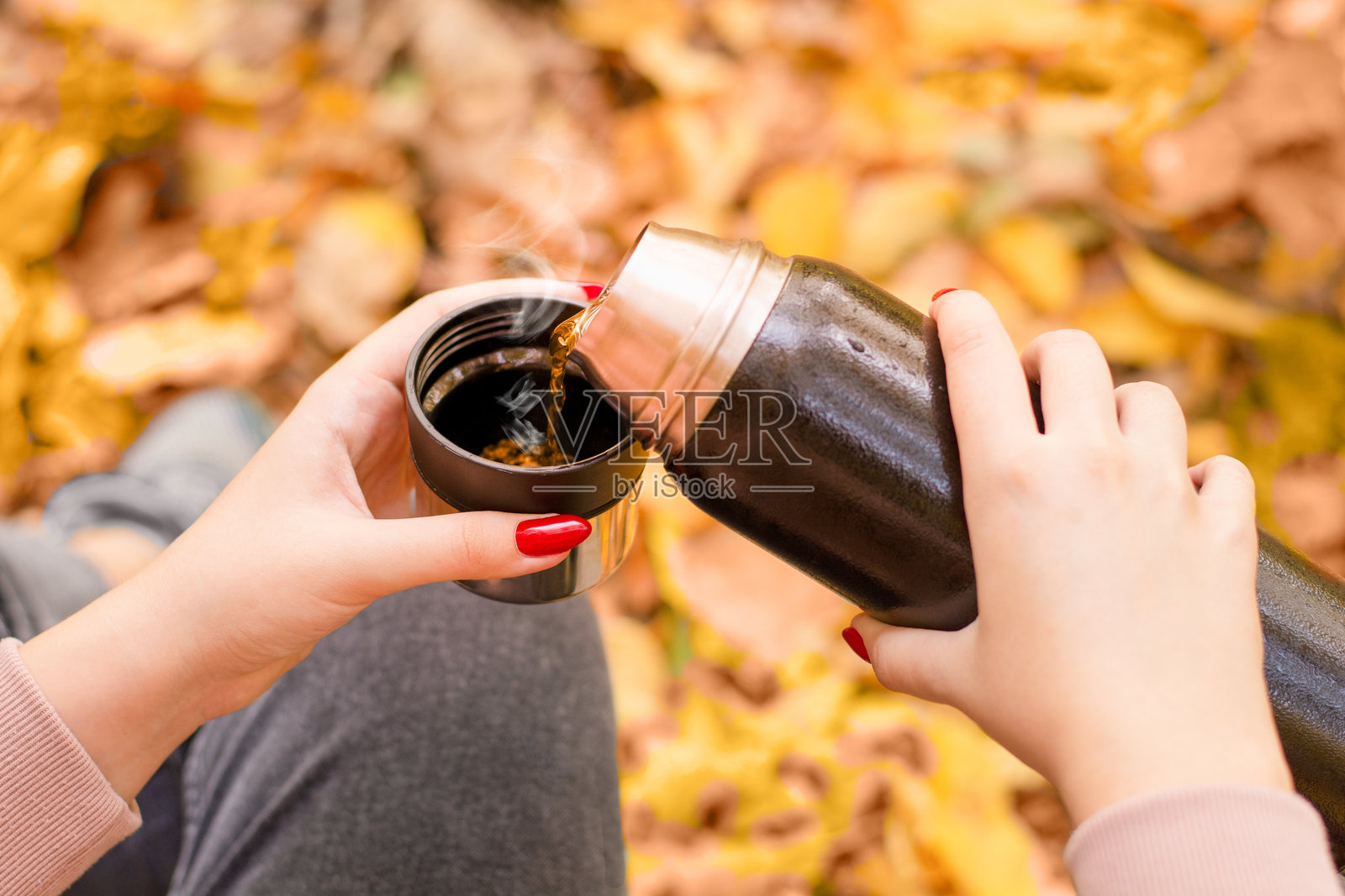 女性手握热茶保温瓶，背景是落下的秋叶照片摄影图片