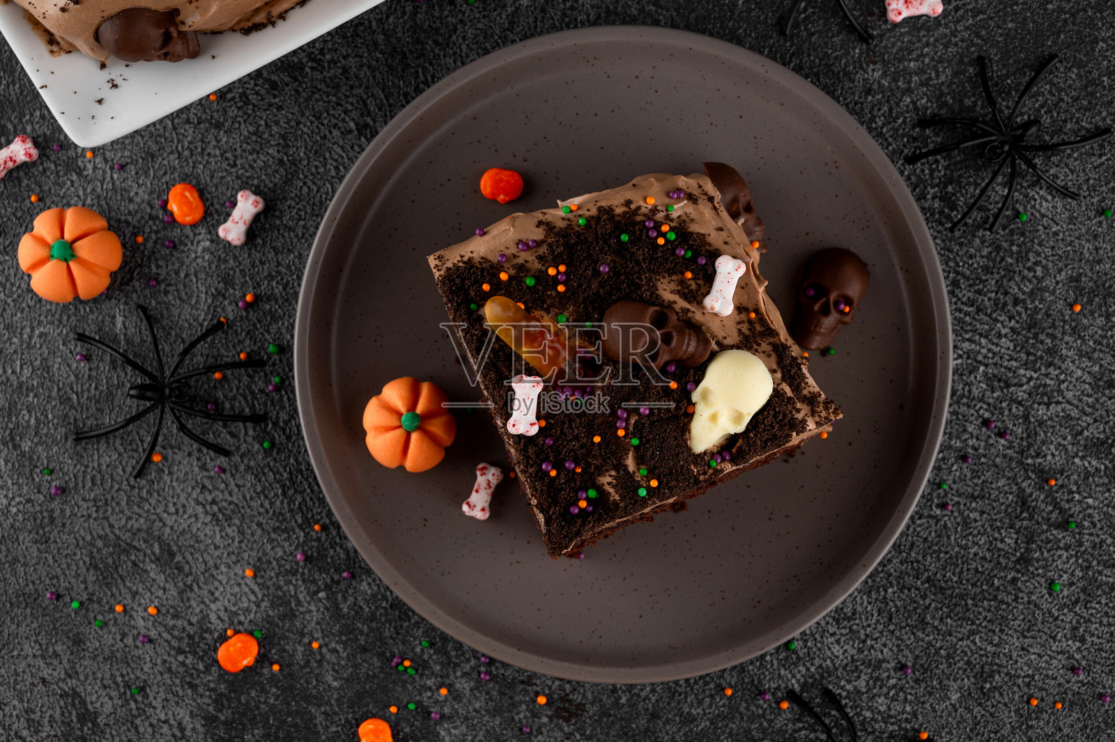 万圣节巧克力蛋糕。脏蛋糕上涂有巧克力奶油，装饰有虫子、骷髅、鬼魂、南瓜和糖霜，背景为黑色。照片摄影图片