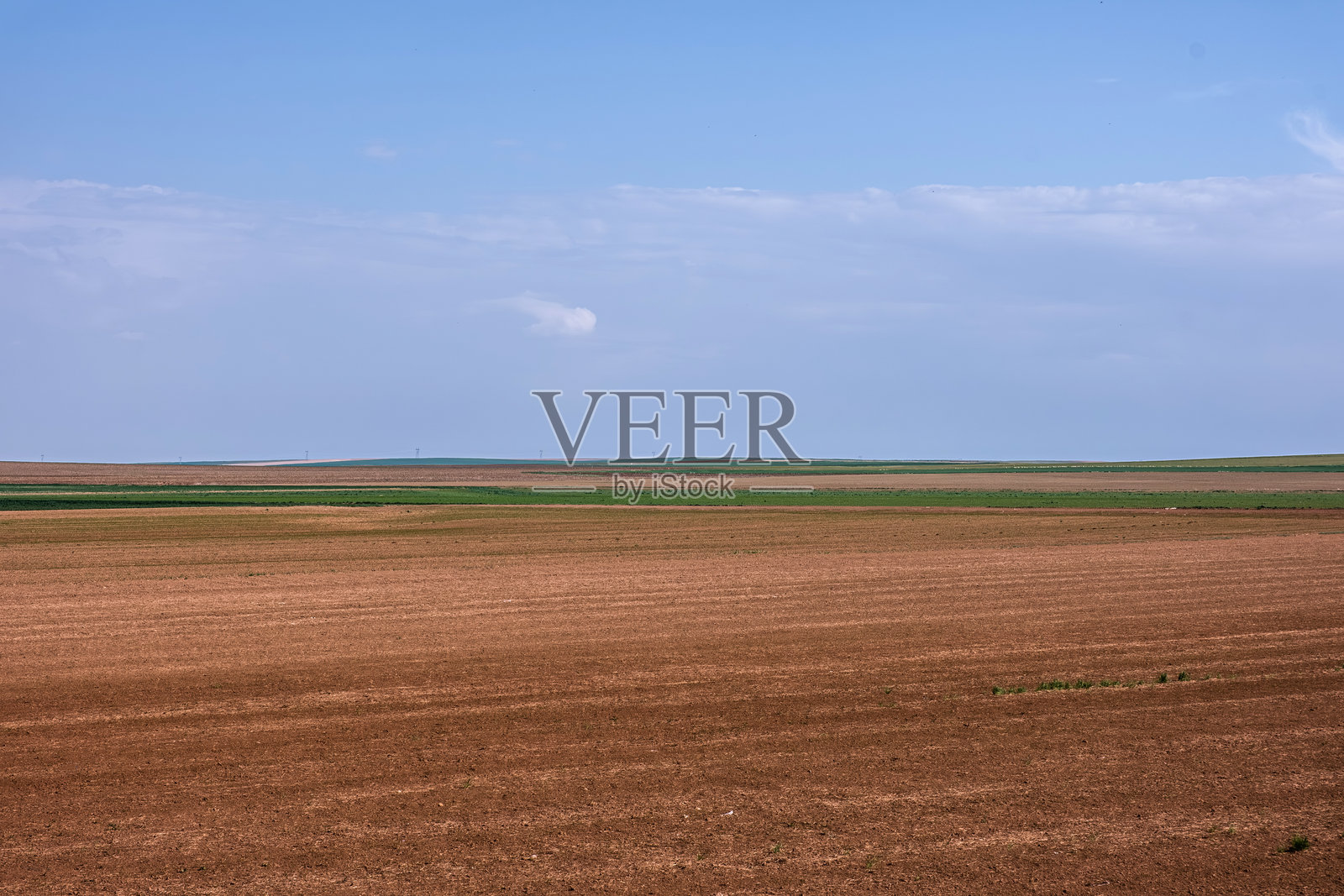 广阔的开阔田野 - 一片平坦的农田在晴朗而广阔的天空下延展，展现了乡村风景的简单与宁静。照片摄影图片