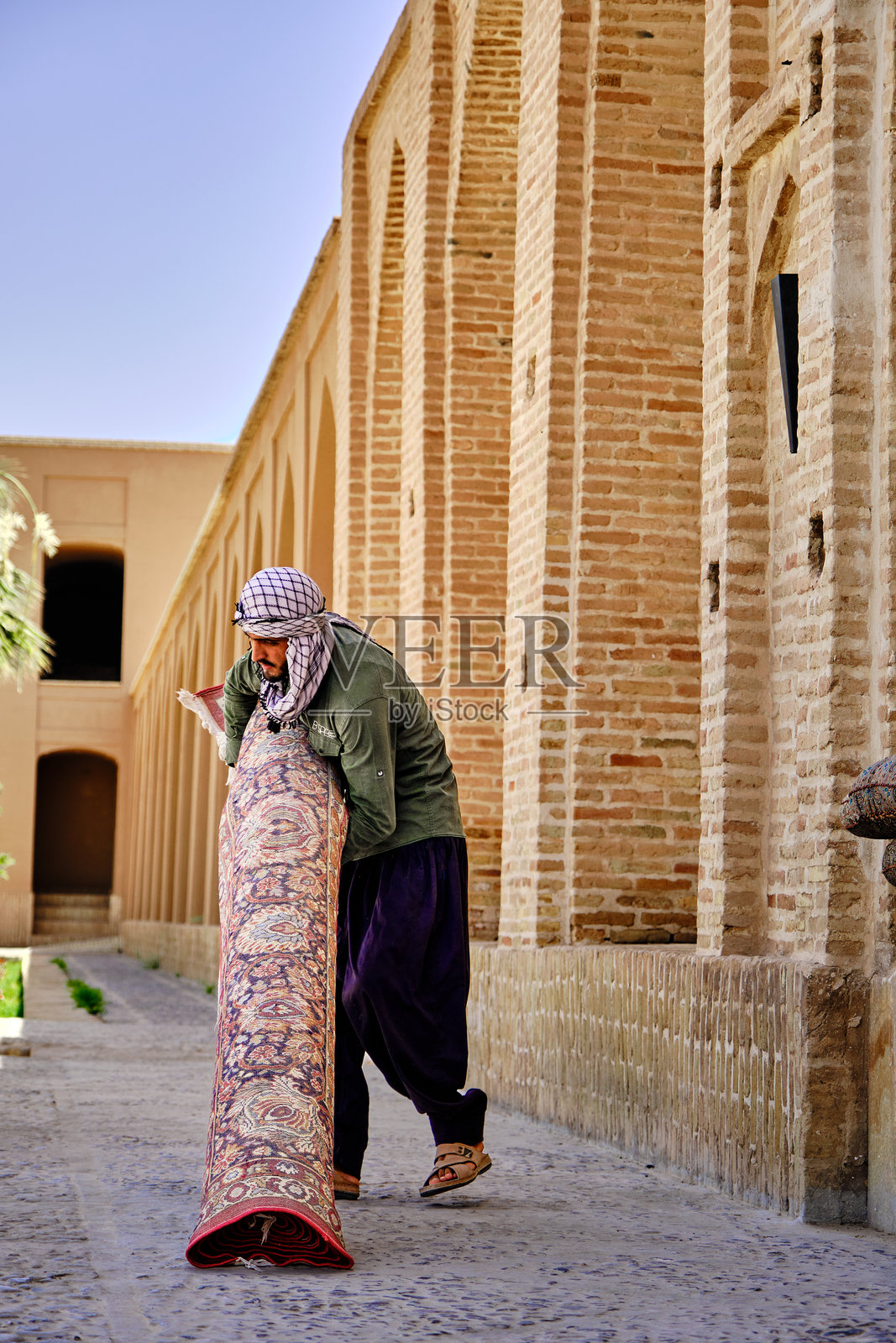 手持伊朗地毯、身穿传统服饰的伊朗男子照片摄影图片