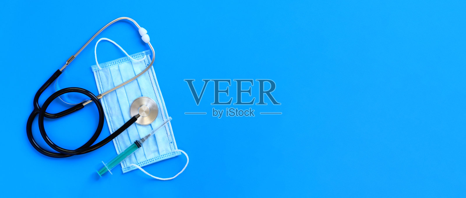 蓝色背景的听诊器，医用防护口罩和注射器照片摄影图片