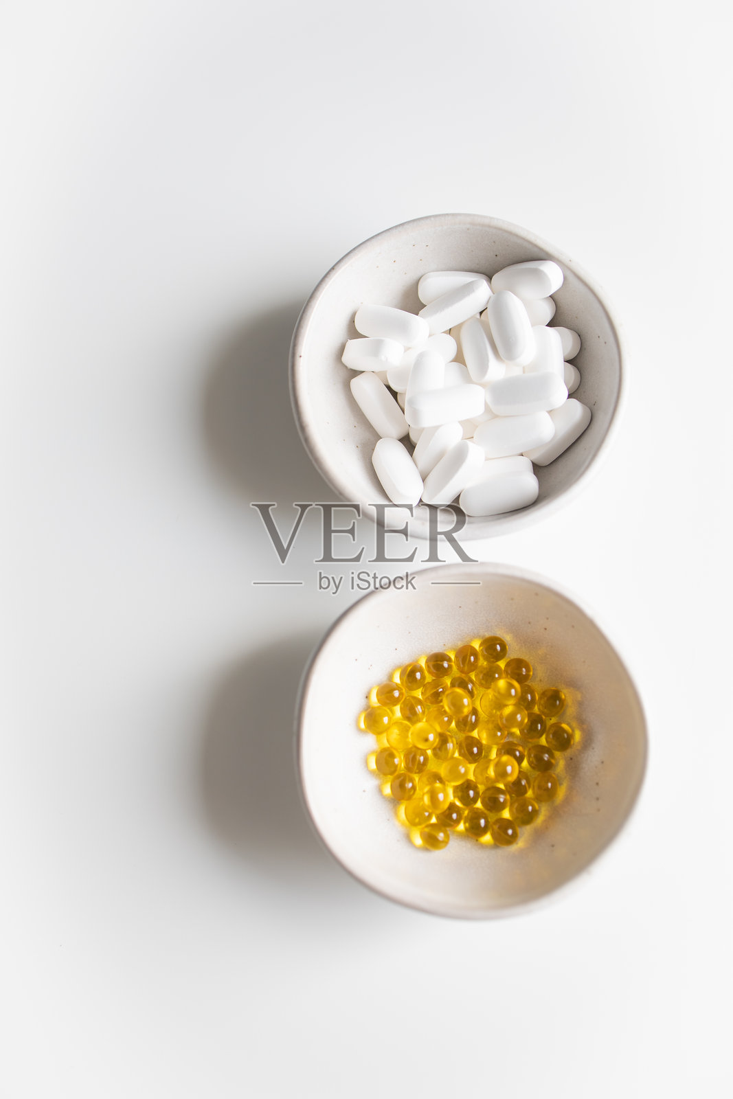 白色和黄色药丸装在白色背景的小碗里照片摄影图片