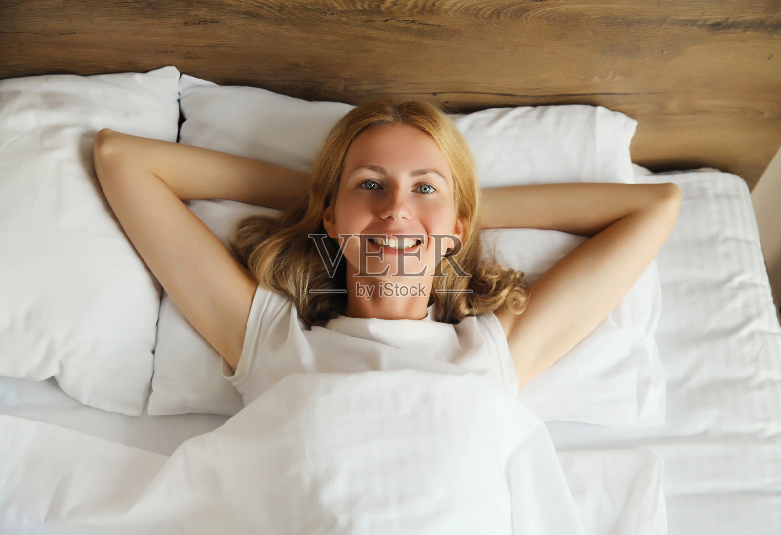 快乐的女人躺在床上，头枕在白色柔软舒适的枕头上，安静地睡觉。照片摄影图片