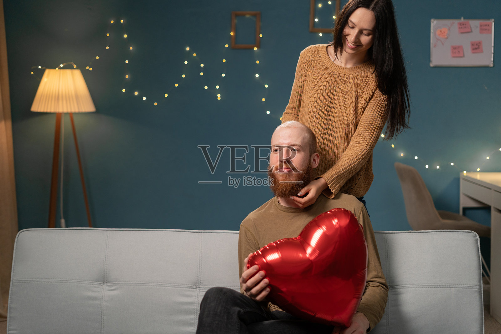 情人节快乐。年轻情侣在家中的客厅里相爱，男人手中拿着心形气球。照片摄影图片