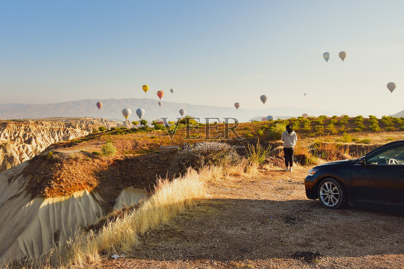 预算女性旅行者坐在折叠露营椅上，观看日出时的热气球。卡帕多奇亚露营与预算旅行概念。照片摄影图片