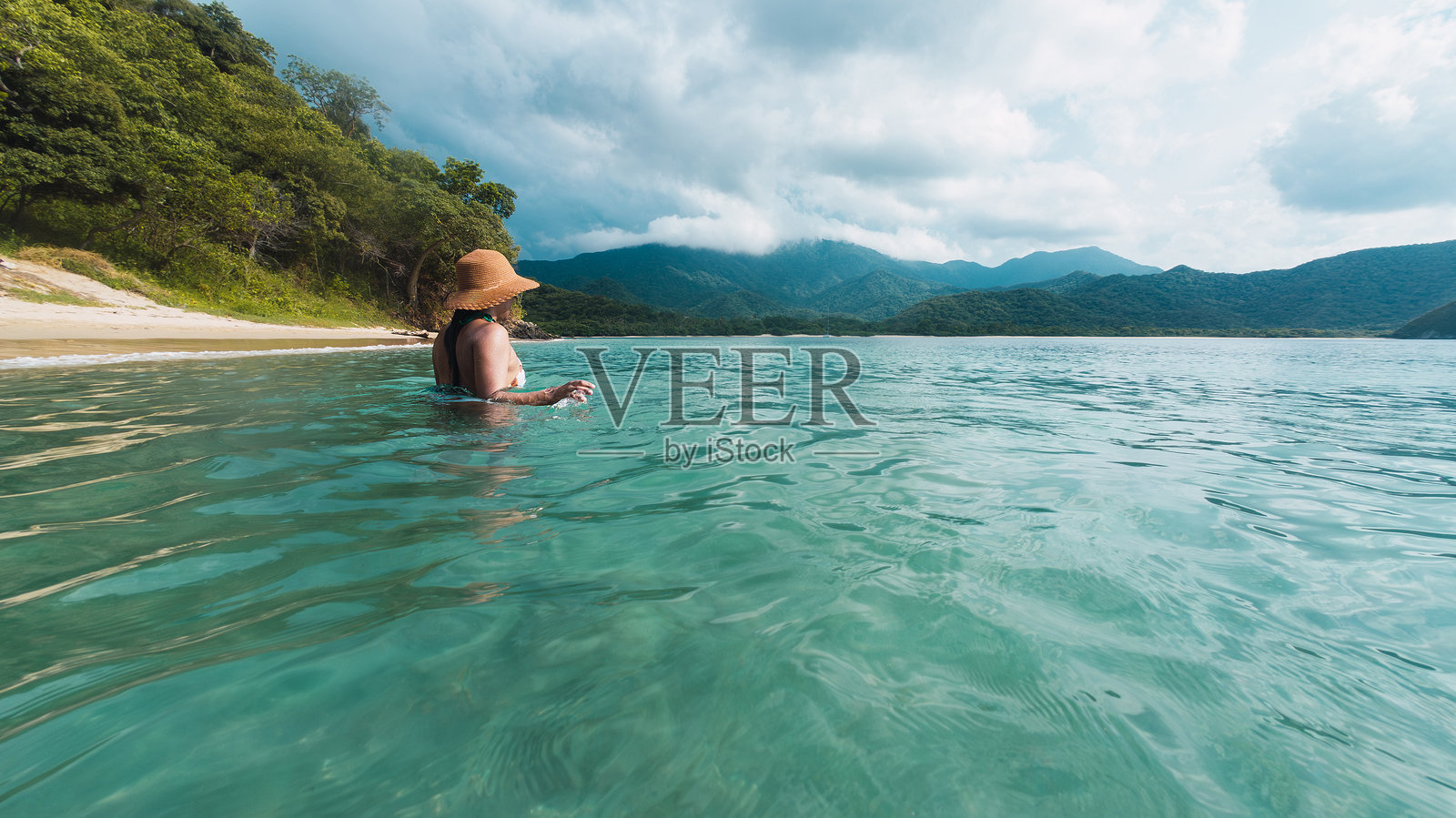女人在清澈的热带水域中畅游，背景是美丽的山景照片摄影图片