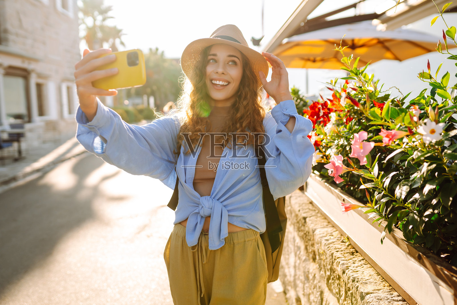 一位年轻女性在阳光明媚的日子里，在风景如画的海滨村庄旁拍摄愉快的自拍照。照片摄影图片