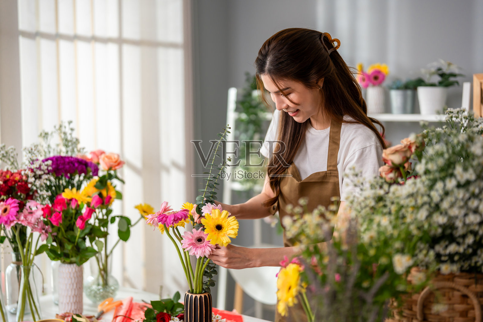 亚洲年轻女花店老板在花店里完成美丽的花束。迷人的女性小企业主感到快乐和放松，为顾客包装花卉礼品。照片摄影图片