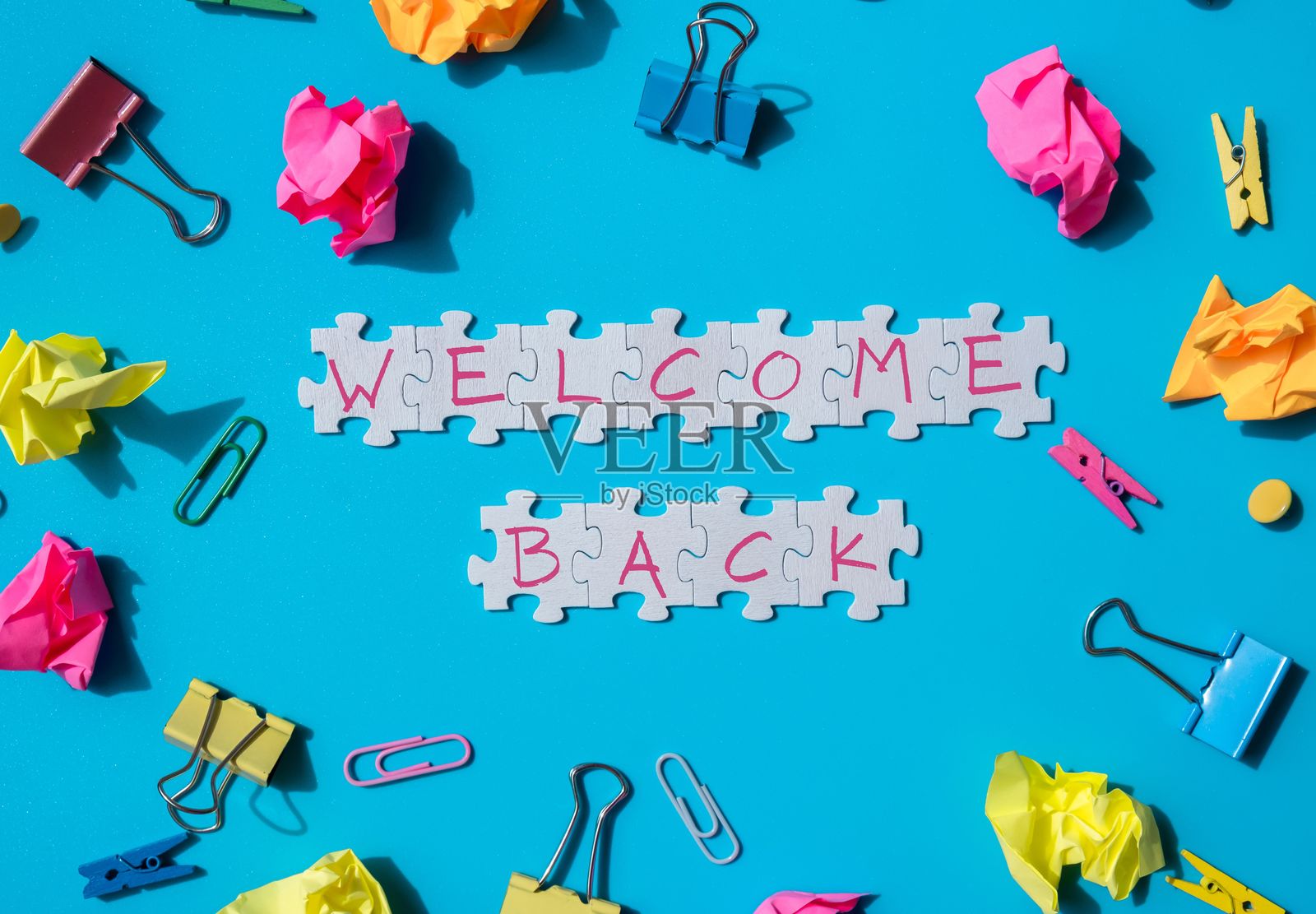 欢迎回到学校的信息铭文，白色拼图上印有创意多彩的蓝色背景，周围是文具用品。面向学生和教师的教育问候公告。俯视平铺视角。照片摄影图片