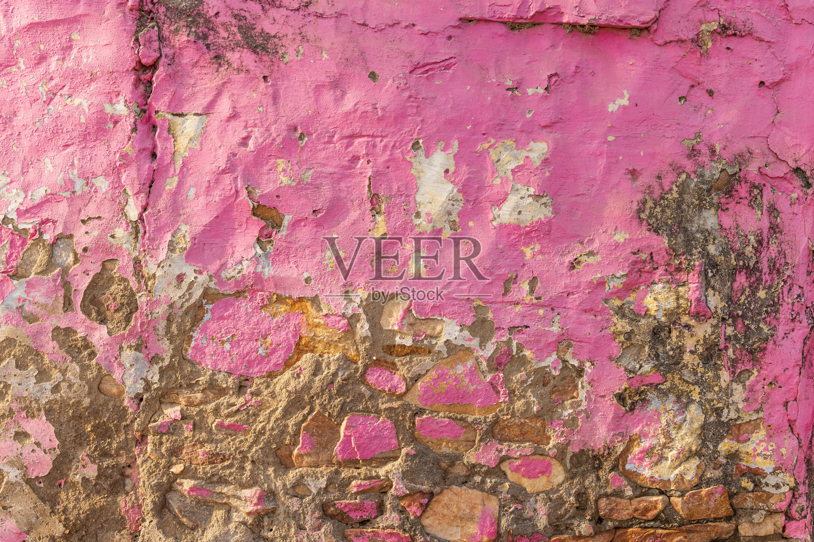 剥落的粉色灰泥墙面上的岩石。照片摄影图片