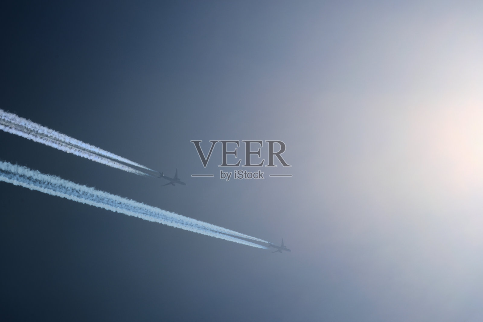 两架飞机朝着太阳飞去。蓝天中的飞机。留有航迹的飞机。照片摄影图片