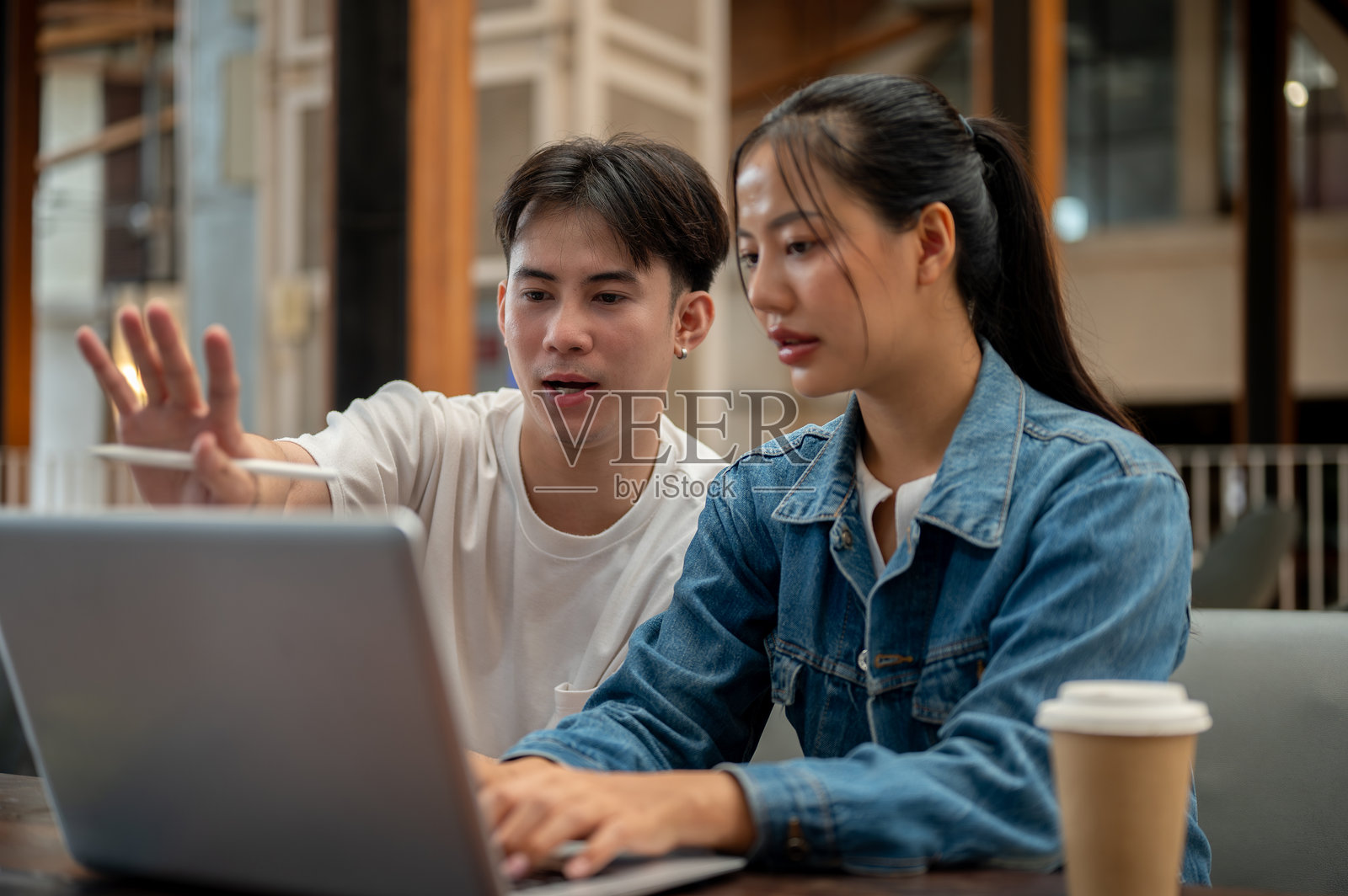 两个积极的亚洲朋友或同事在咖啡店里远程合作。照片摄影图片