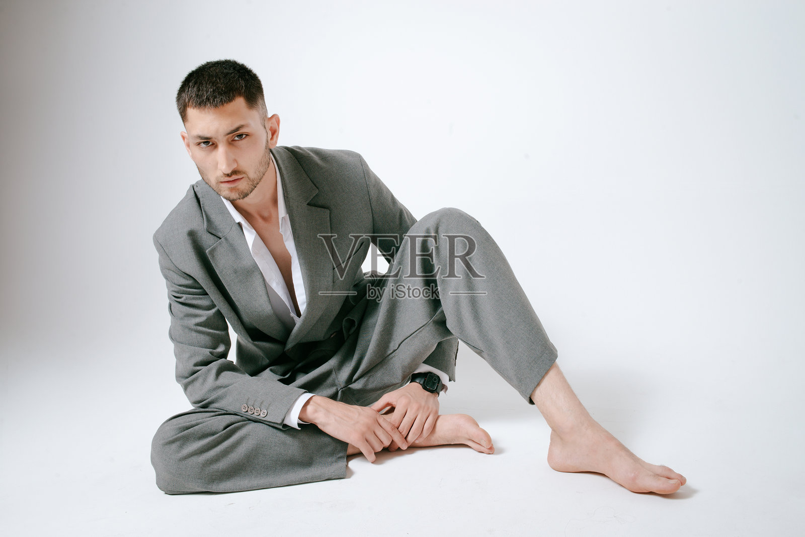 穿着灰色西装的帅气男子赤脚坐在地板上照片摄影图片