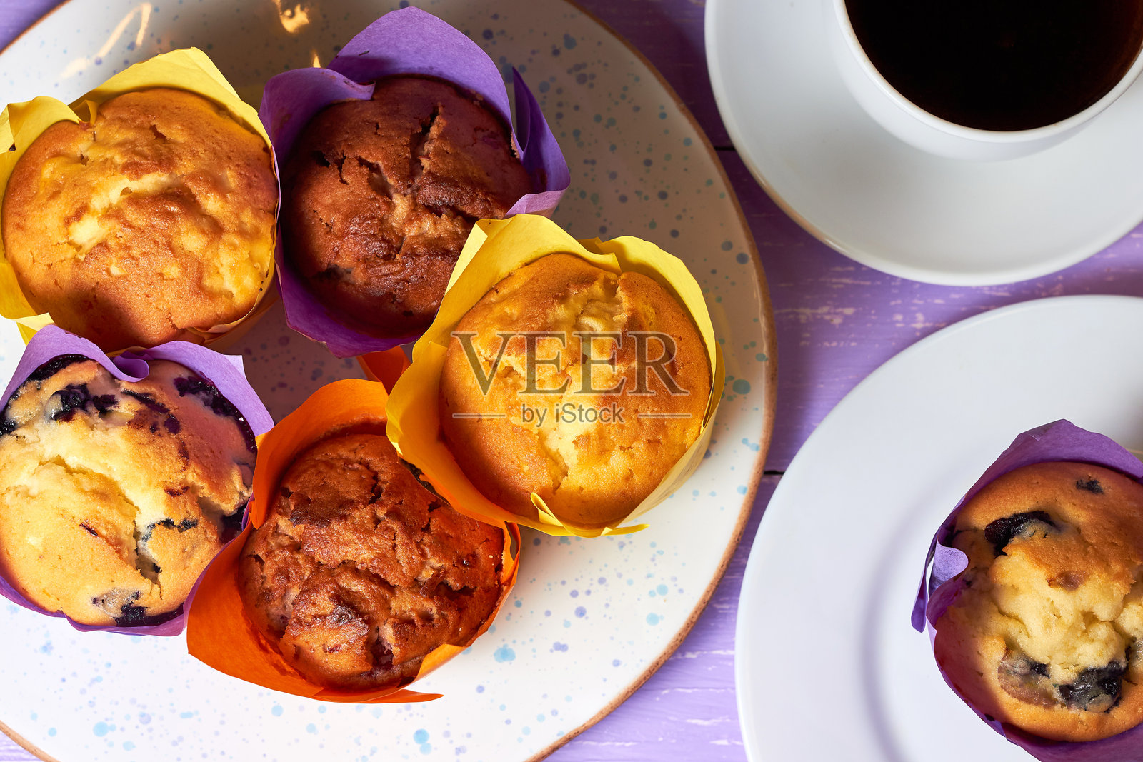 从上方俯视紫色桌面上的甜美松饼、杯子蛋糕和一杯咖啡照片摄影图片