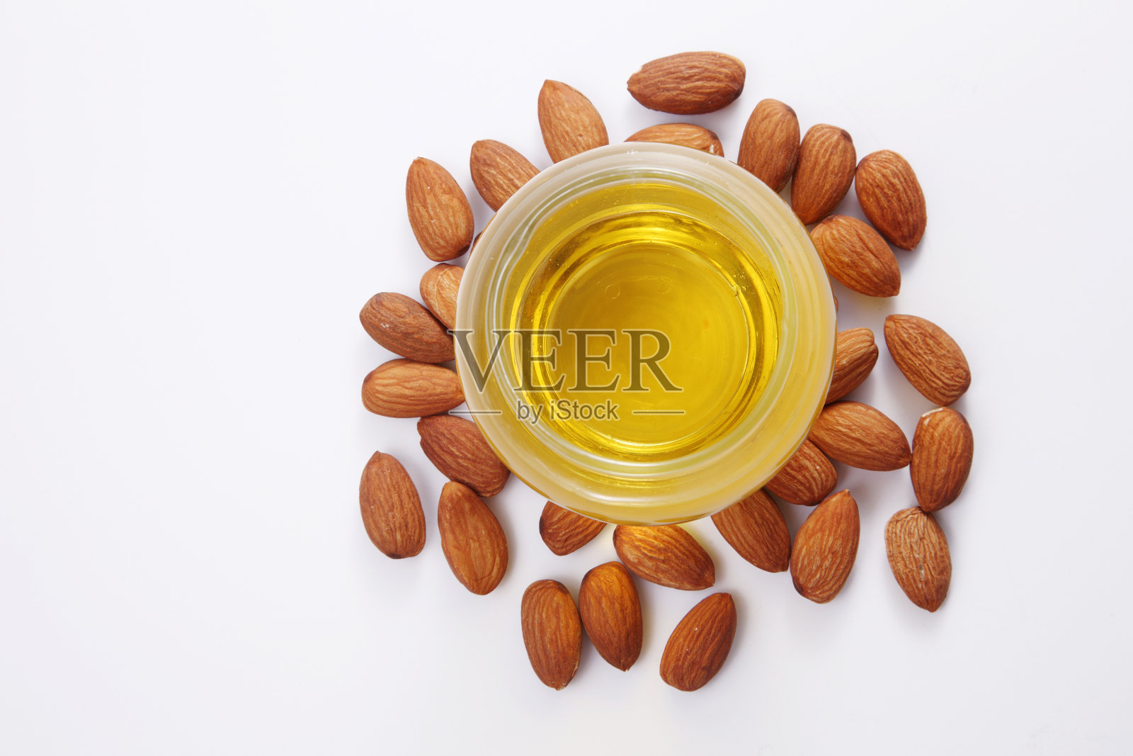白色背景下，碗中盛有烹饪油，周围环绕着杏仁的特写镜头照片摄影图片