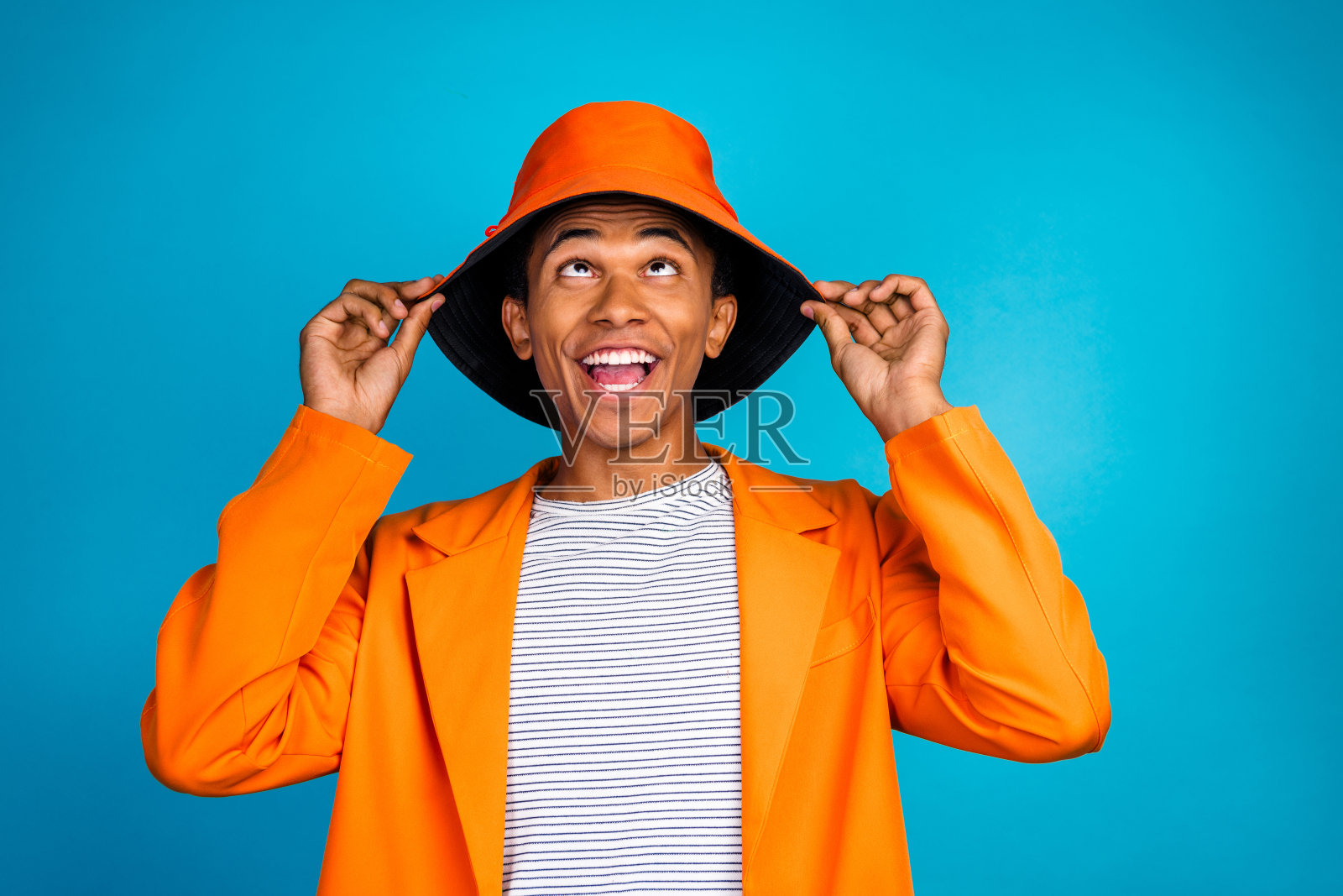 穿着橙色时尚帽子的积极疯狂的家伙，背景是蓝色青色。照片摄影图片