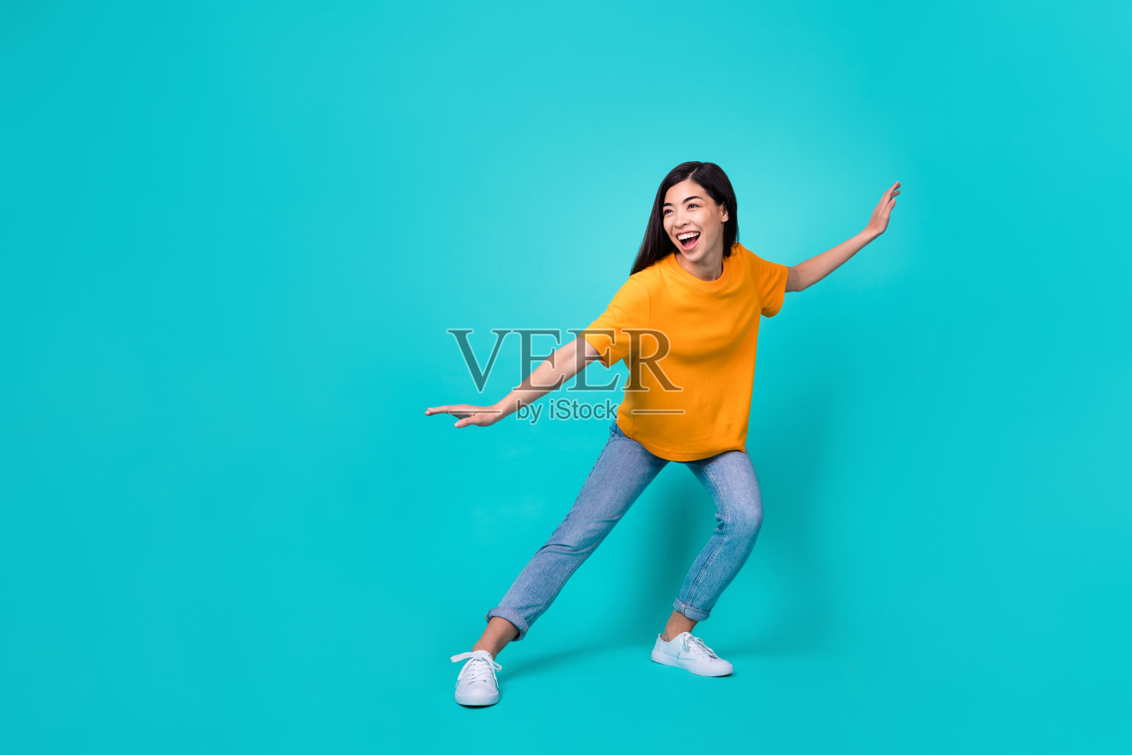 全身照，漂亮的棕发女士穿着促销T恤、牛仔裤和鞋子，背景为青色。照片摄影图片