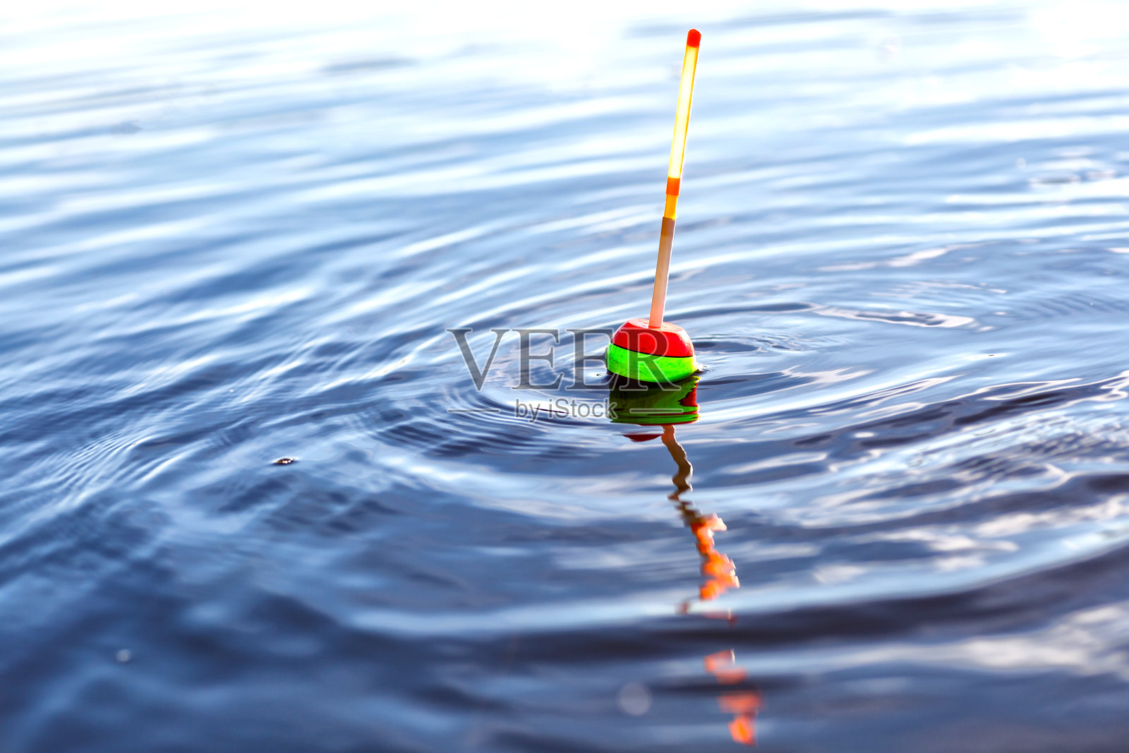 水面上的钓鱼浮漂周围有圈圈。钓鱼冒险，鲤鱼钓鱼。捕捉鱼类。蓝天倒映在水中，鱼在咬钩。照片摄影图片