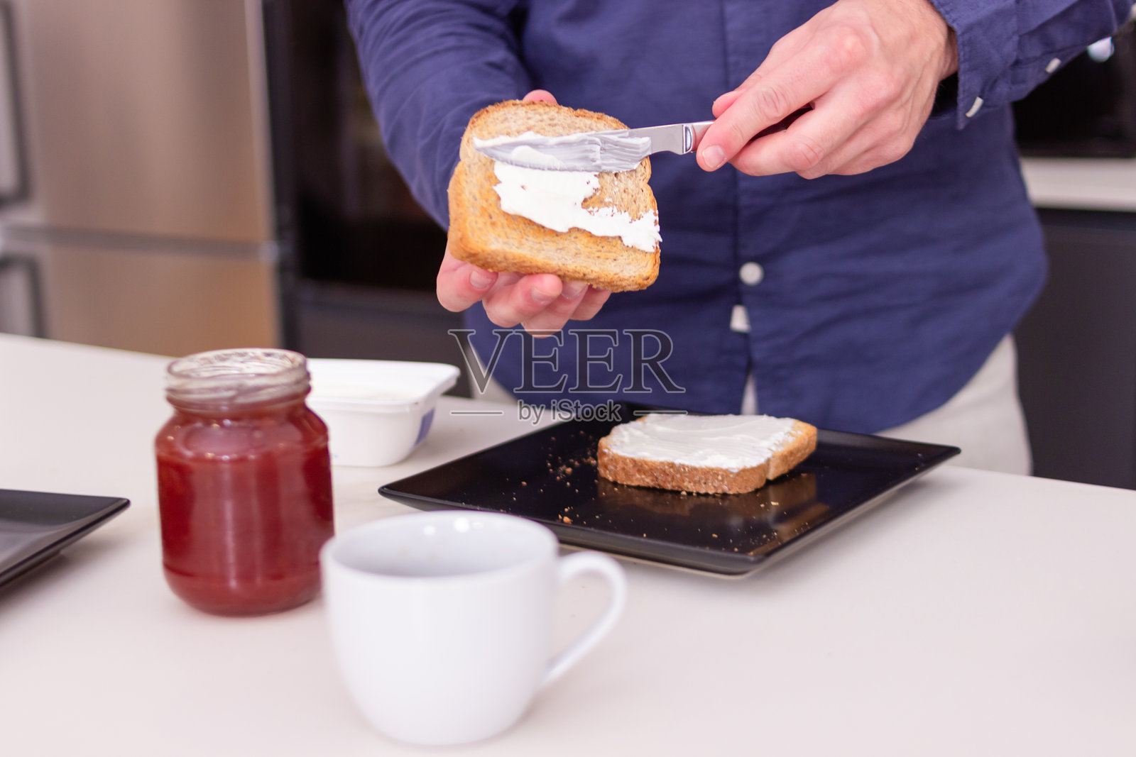 男人在厨房里给吐司涂抹奶油奶酪作为早餐照片摄影图片