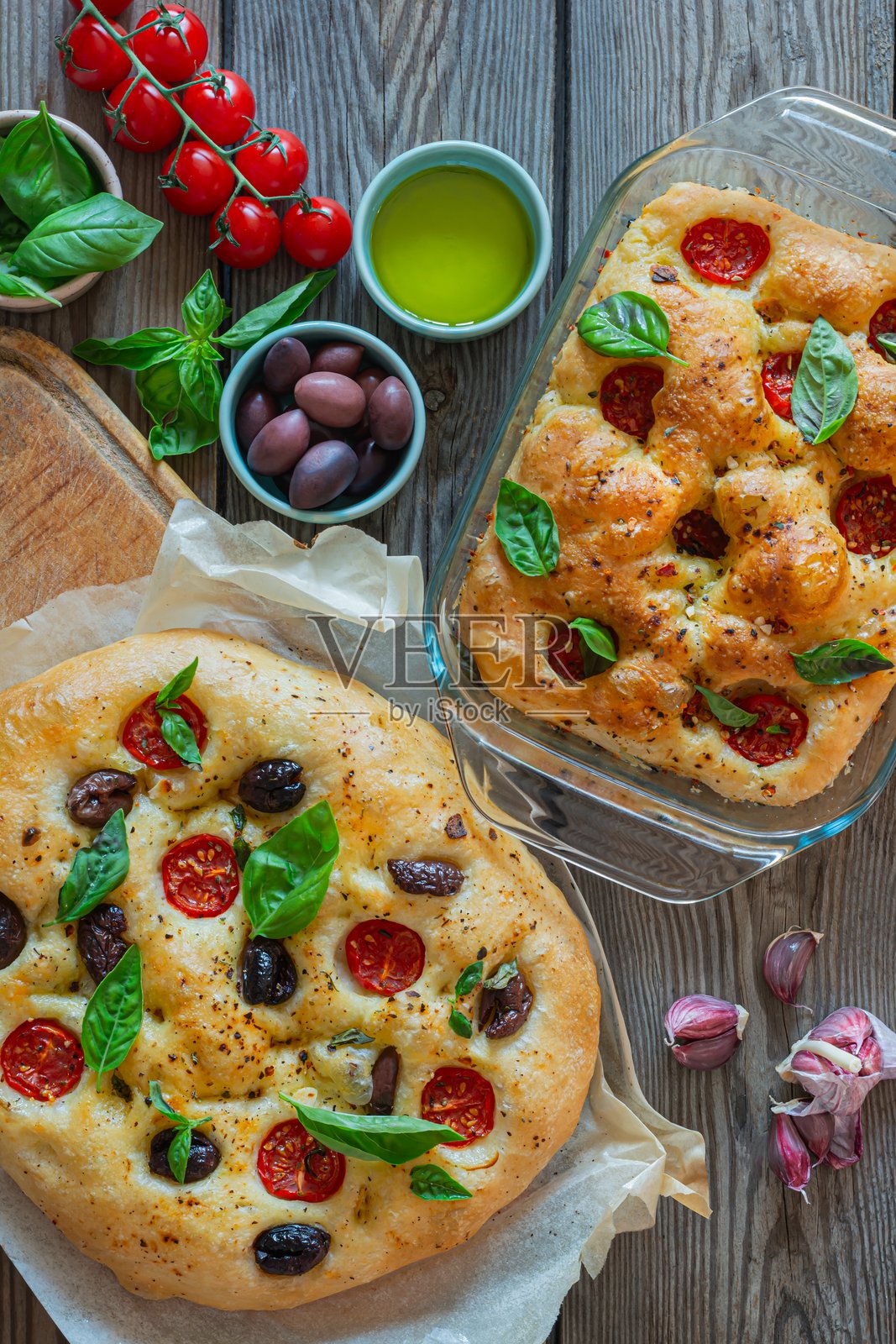 新鲜意大利平面面包佛卡夏，上面放有番茄、橄榄、大蒜和香草，背景为木质纹理。照片摄影图片