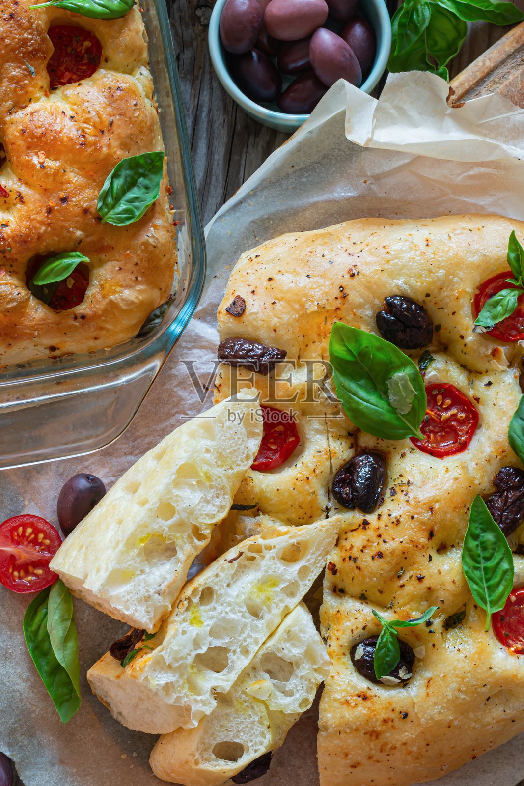 新鲜意大利平面面包佛卡夏，上面放有番茄、橄榄、大蒜和香草，背景为木质纹理。照片摄影图片