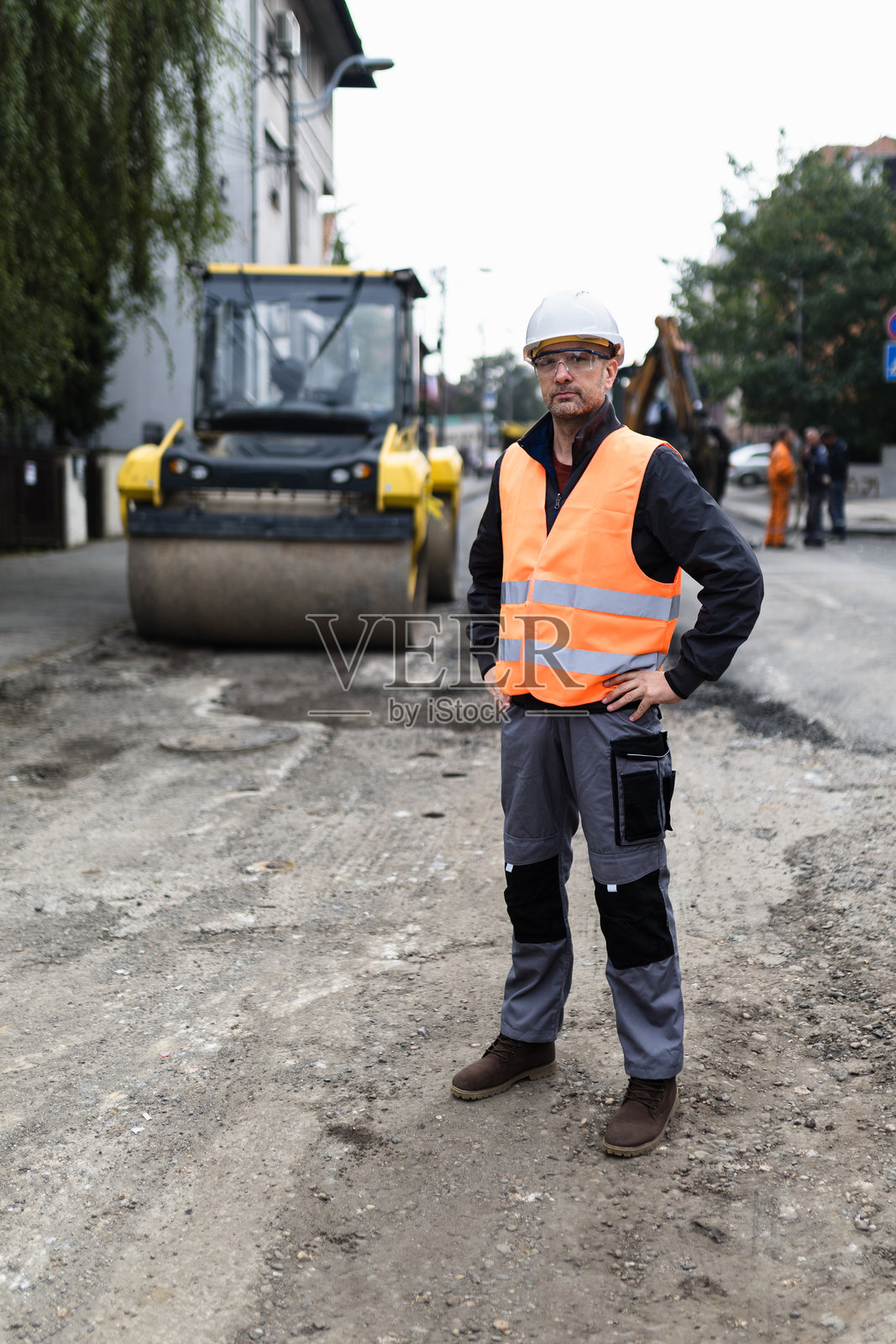 穿着安全背心的建筑工人在阴云密布的天气中监督繁忙城市街道的道路修复项目照片摄影图片