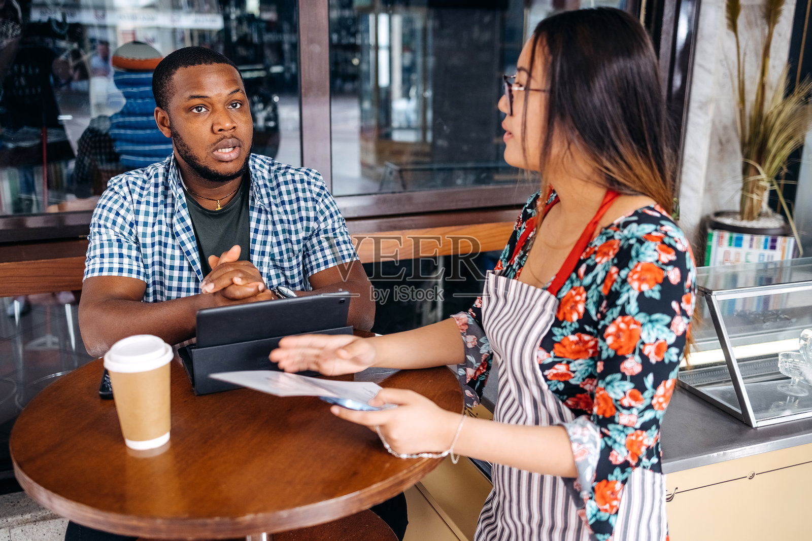 亚洲女服务员在咖啡馆为常客推荐点餐。照片摄影图片