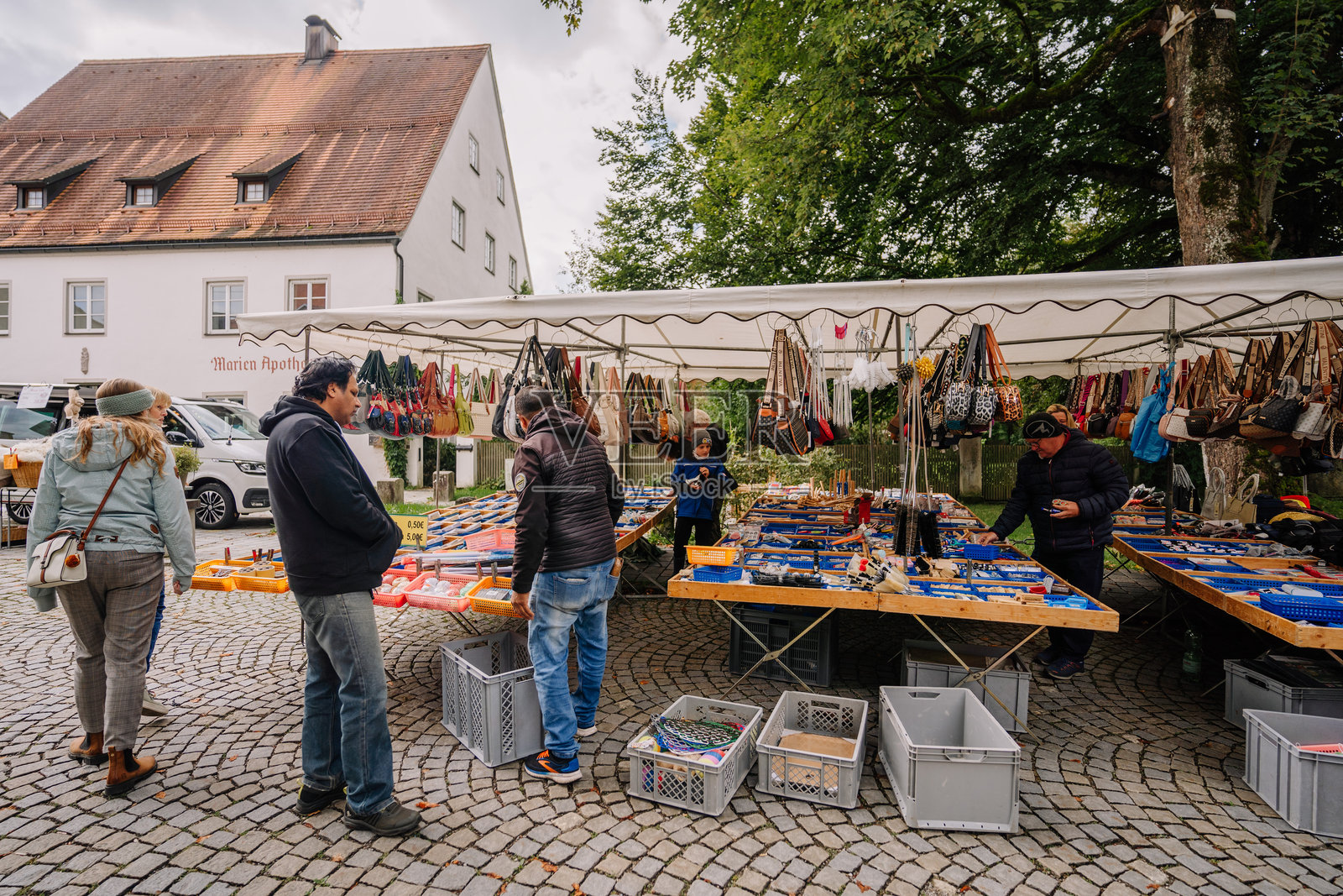 一个繁忙的户外市场摊位，出售各种工具、配件和手袋，许多人在巴伐利亚浏览商品。照片摄影图片