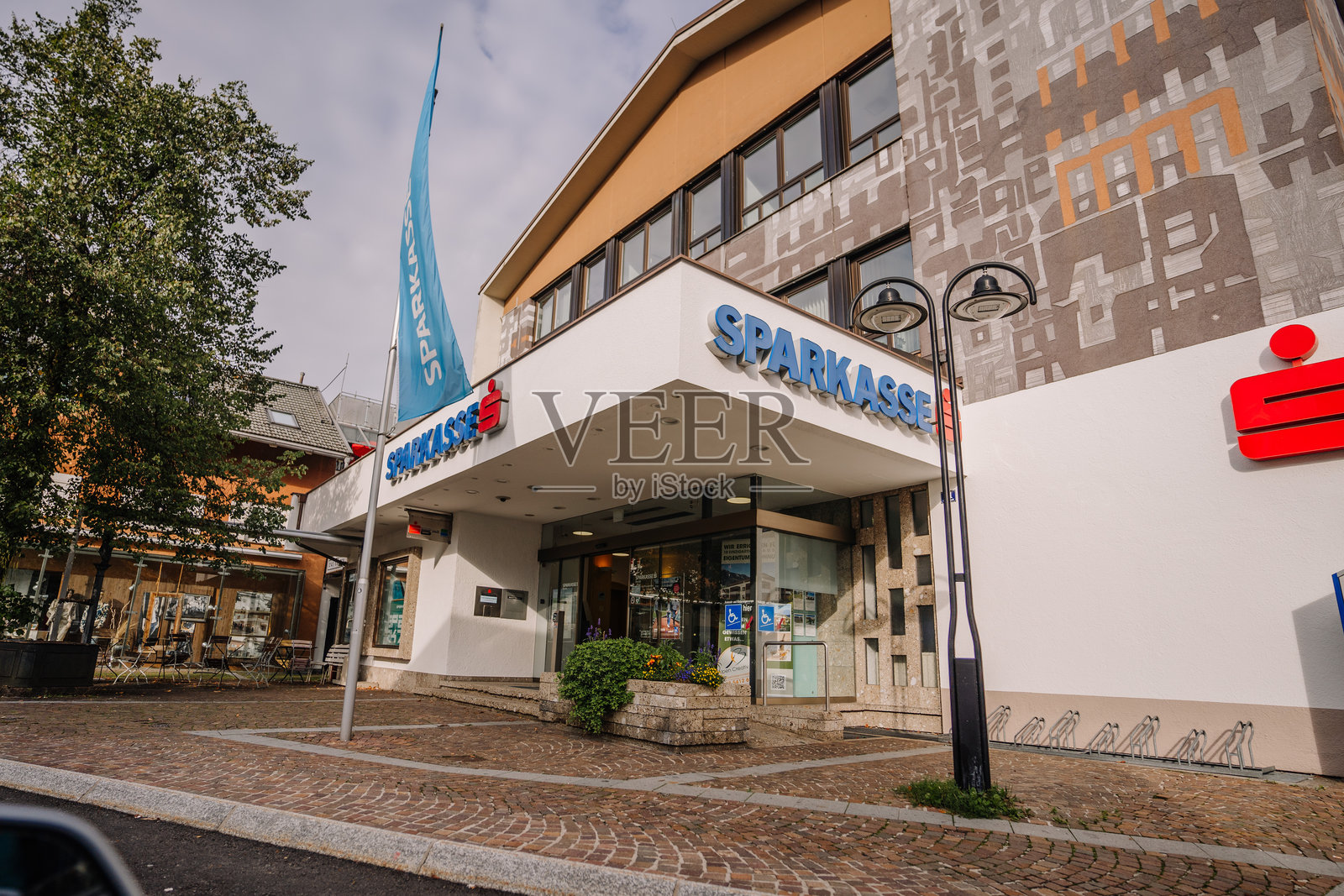 一座现代化的Sparkasse银行建筑，前面有一个大招牌、旗帜和砖石铺成的人行道，位于一个欧洲小镇的阴 cloudy sky。照片摄影图片