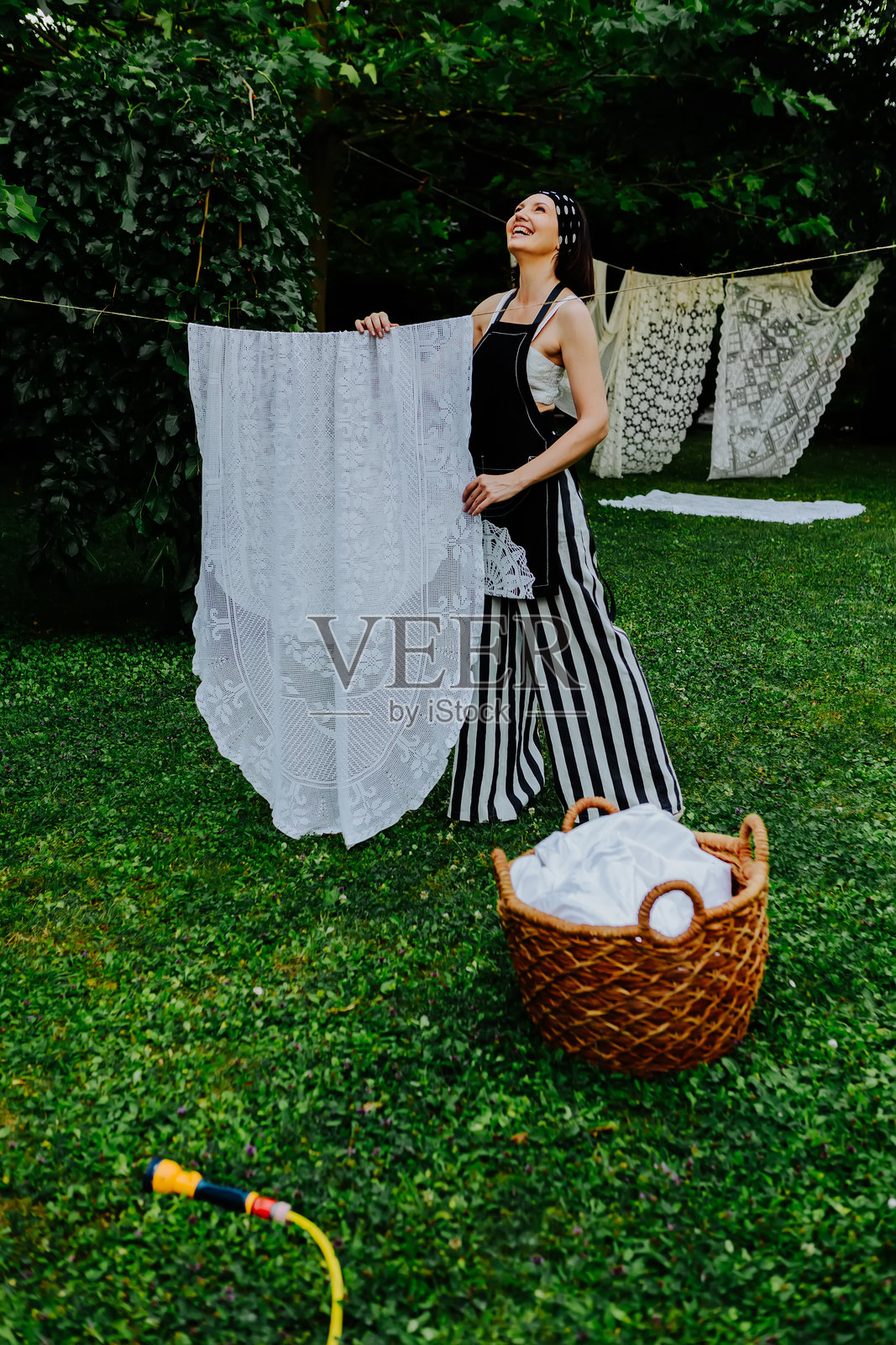 女人在郁郁葱葱的花园里，正在晾晒精美的蕾丝布料。照片摄影图片