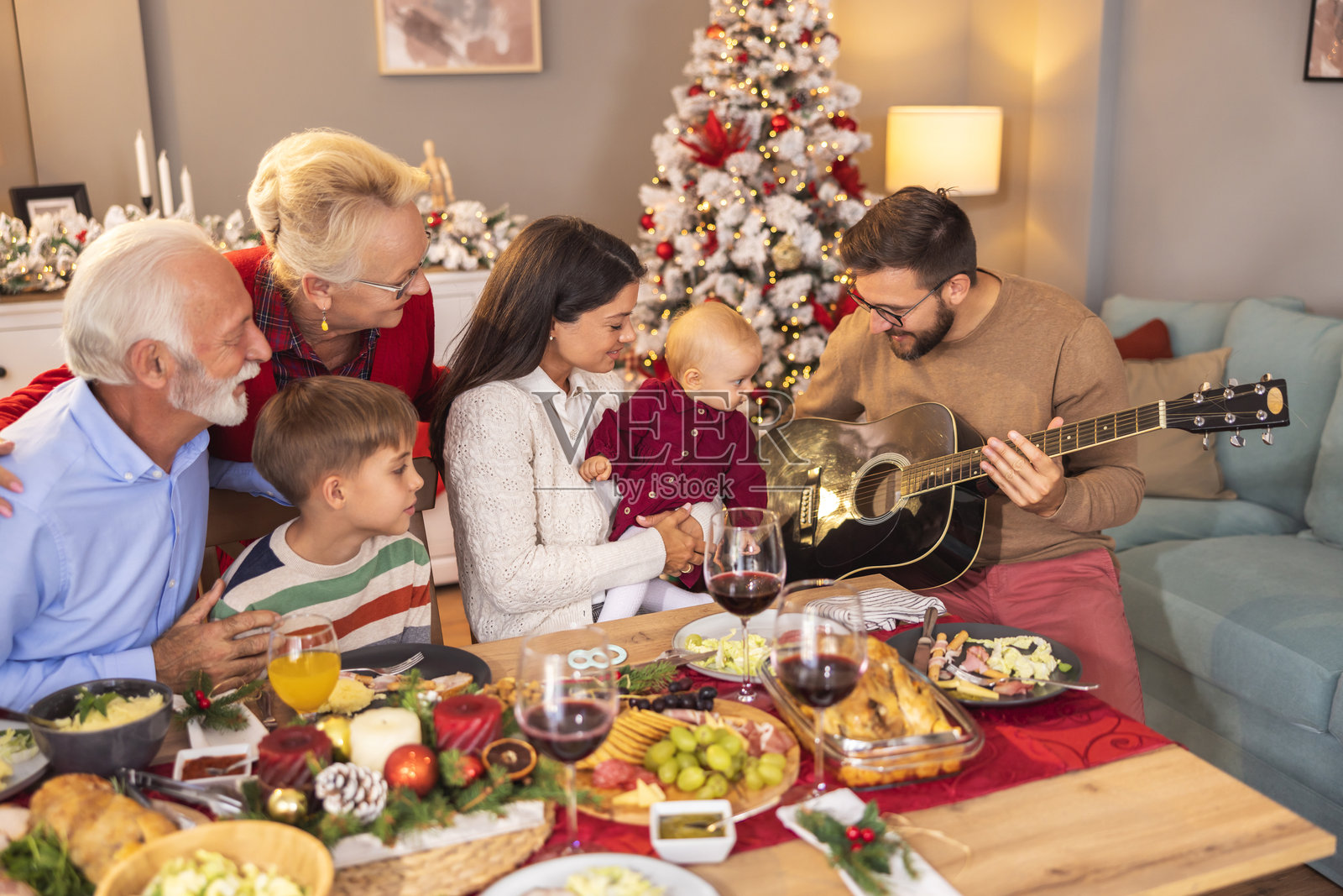 年轻人在家庭圣诞晚餐上弹吉他照片摄影图片