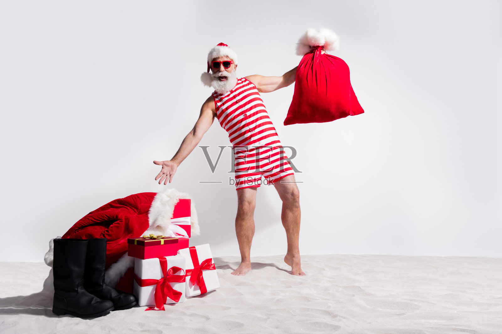快乐的圣诞老人穿着红色泳衣和太阳镜，旅行夏日之旅，背景是白色沙滩。照片摄影图片