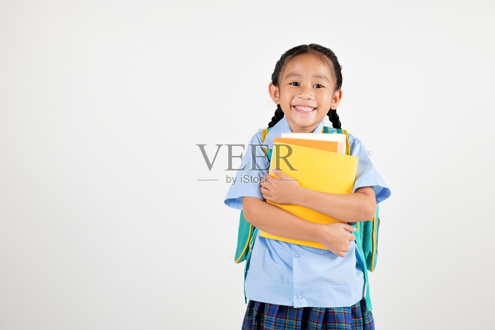 微笑的亚洲小女孩在幼儿园里，手里抱着书包和书籍，背景为白色，快乐可爱的小学生穿着校服，准备返校。照片摄影图片