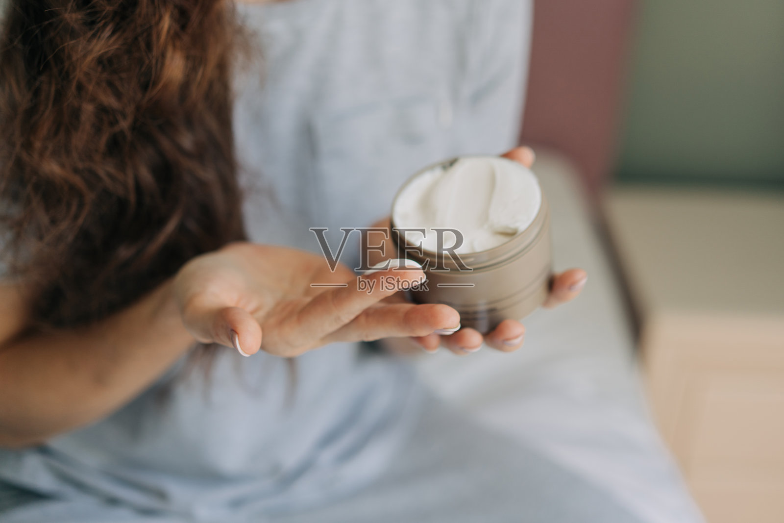 一位面目模糊的女性手持一瓶护肤霜，并在手上涂抹护肤霜。照片摄影图片