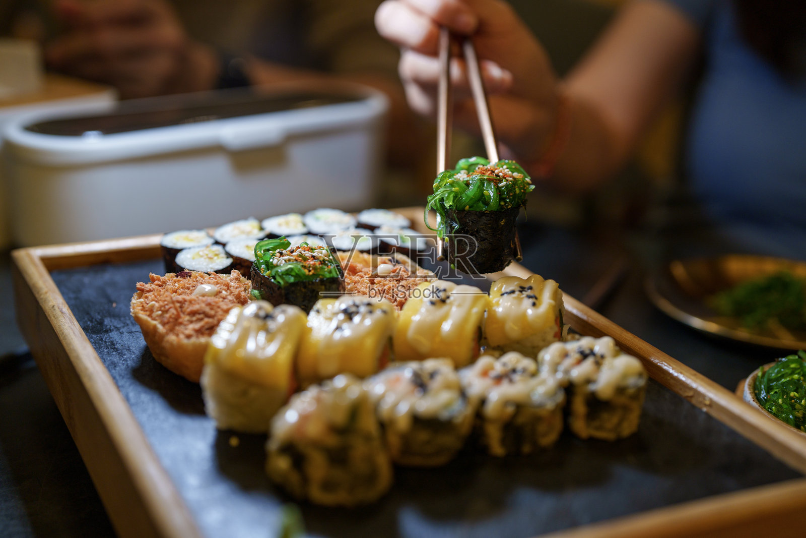一位女性的手在素食餐厅中伸向一盘素食寿司的特写。照片摄影图片