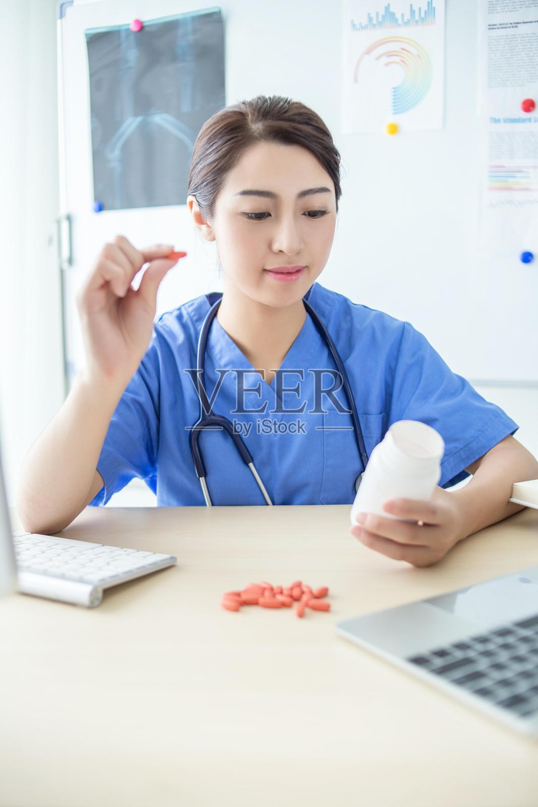 亚洲女性医生佩戴听诊器，手持药瓶，正看着洒落在桌子上的药片。照片摄影图片