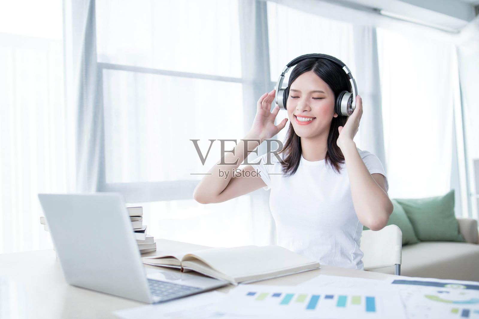 微笑的少女戴着耳机使用笔记本电脑，科技与休闲的概念照片摄影图片