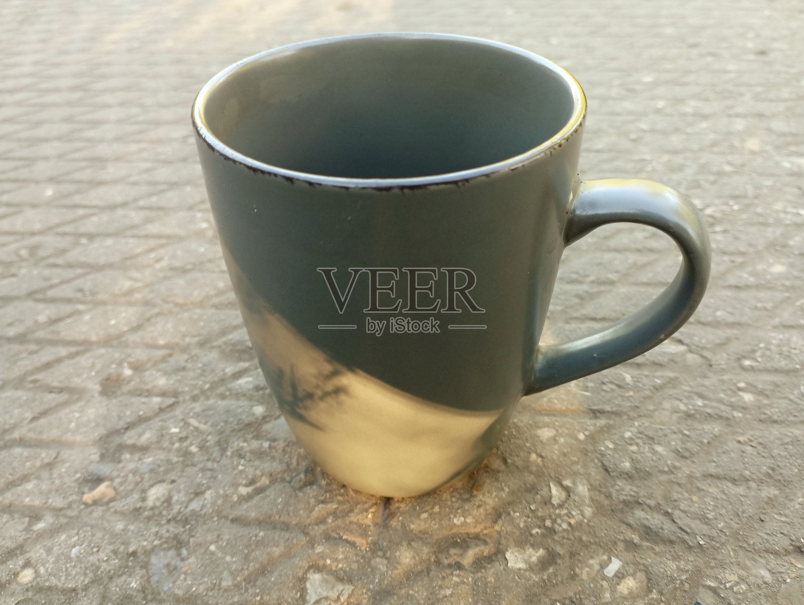 一个灰色的杯子放在户外的混凝土底座上。深灰色的餐具适合热饮和冷饮。照片摄影图片