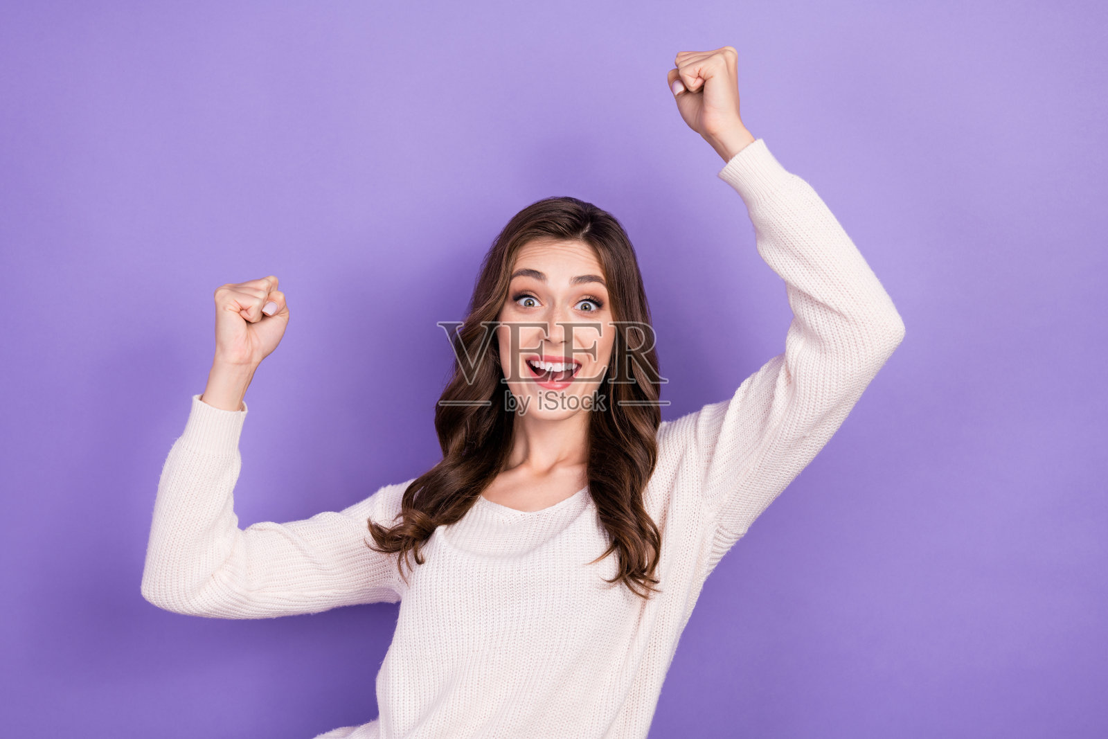 兴奋的棕发女性在淡紫色背景下举手庆祝终于迎来周末假期，展现出活力四射的风格。照片摄影图片