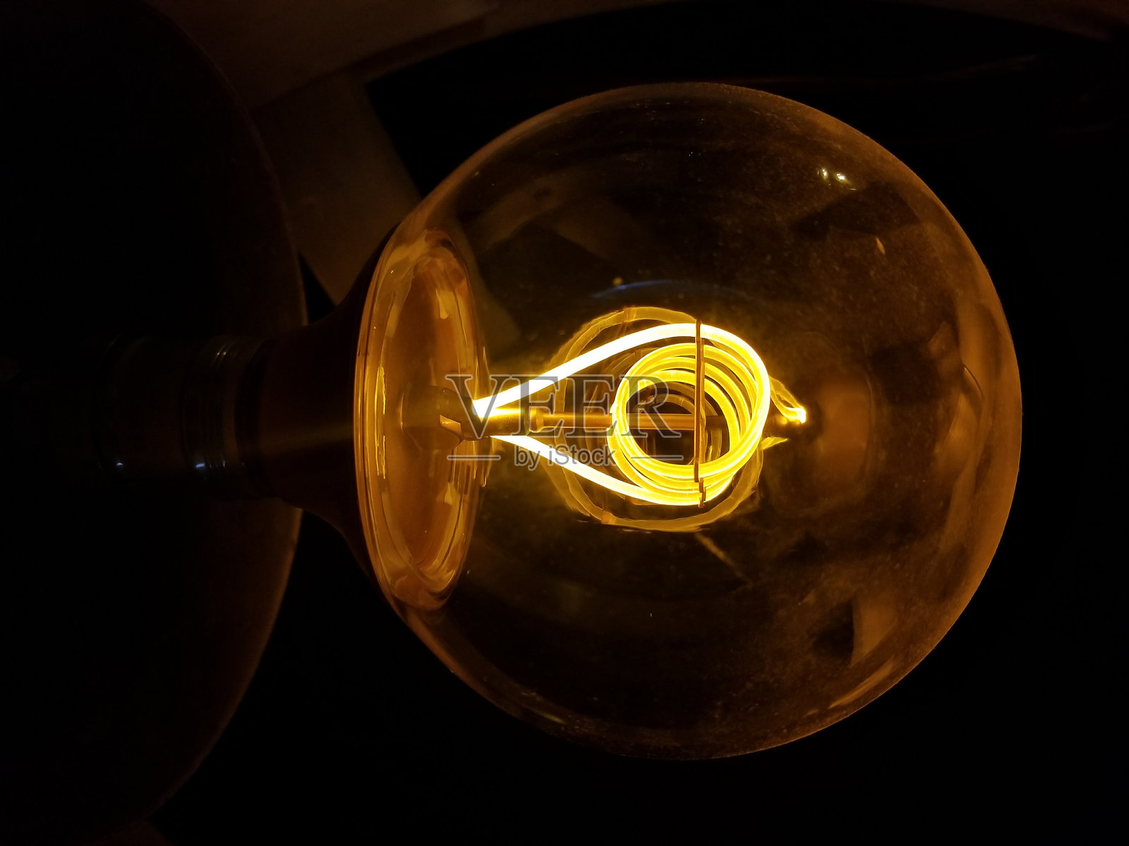 一个发光的复古灯泡在傍晚照亮黑暗空间，灯丝设计复杂。照片摄影图片