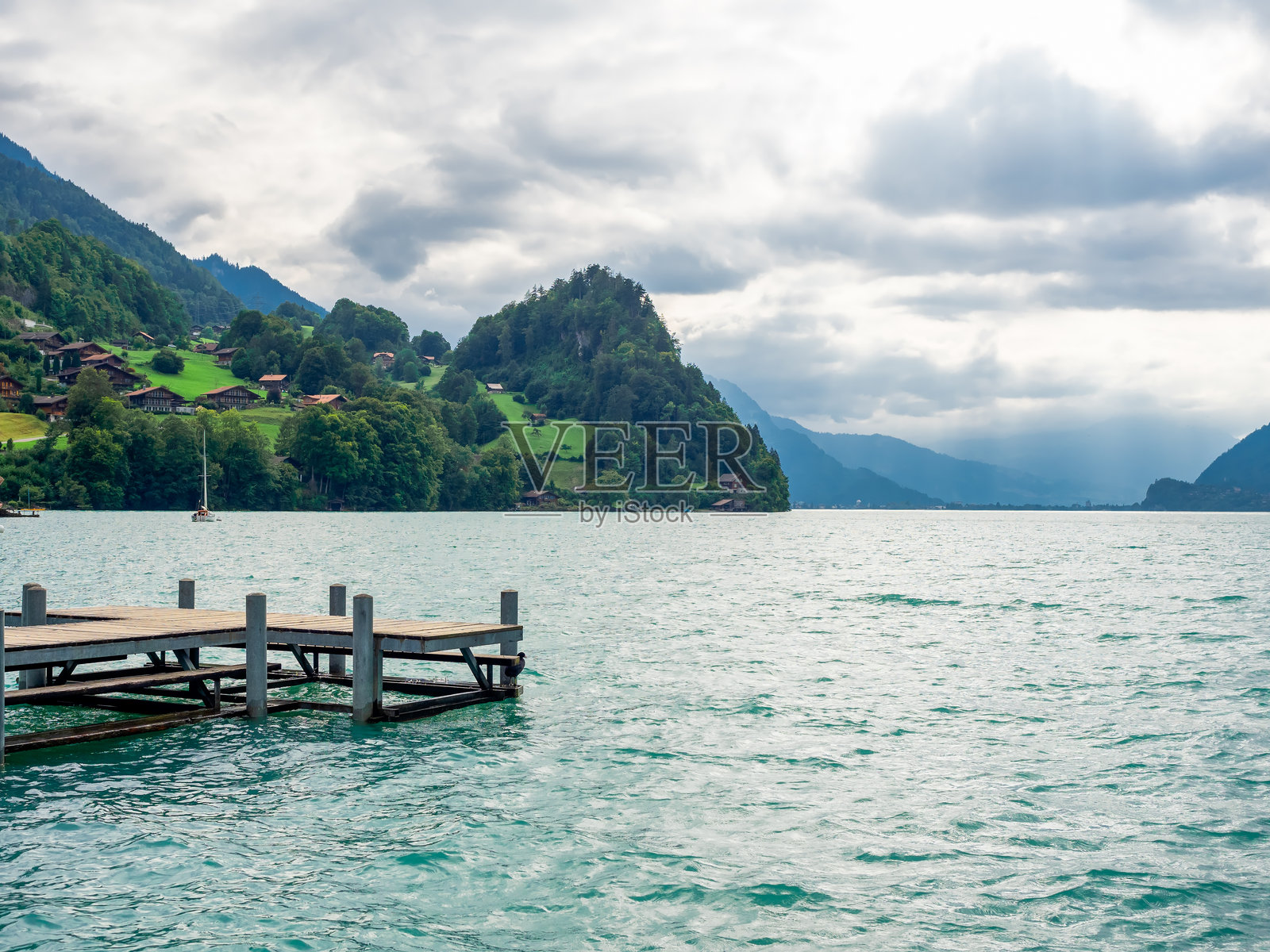 空荡荡的木栈桥，湖滨无人，绿丘上的村庄、山脉和水面在夏季多云的天空背景下。瑞士伊塞尔特瓦尔德的著名景点。照片摄影图片