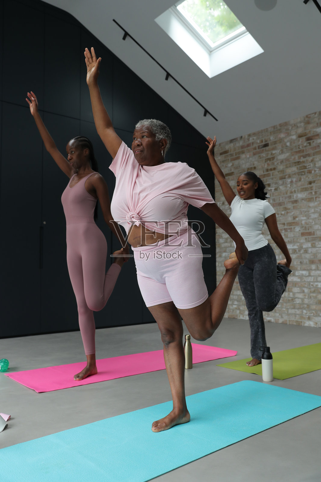 三位微笑的女性在瑜伽馆的瑜伽垫上练习纳塔拉贾萨那姿势。照片摄影图片