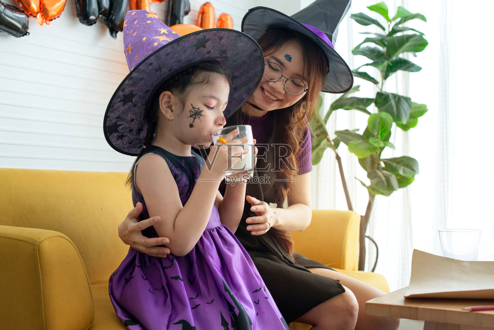 穿着万圣节服装的小女孩正在喝牛奶。照片摄影图片