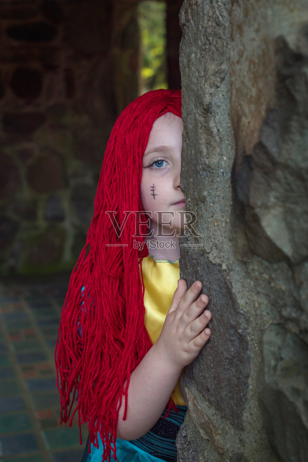 有趣的躲猫猫游戏：红发7岁女孩藏在石墙后照片摄影图片