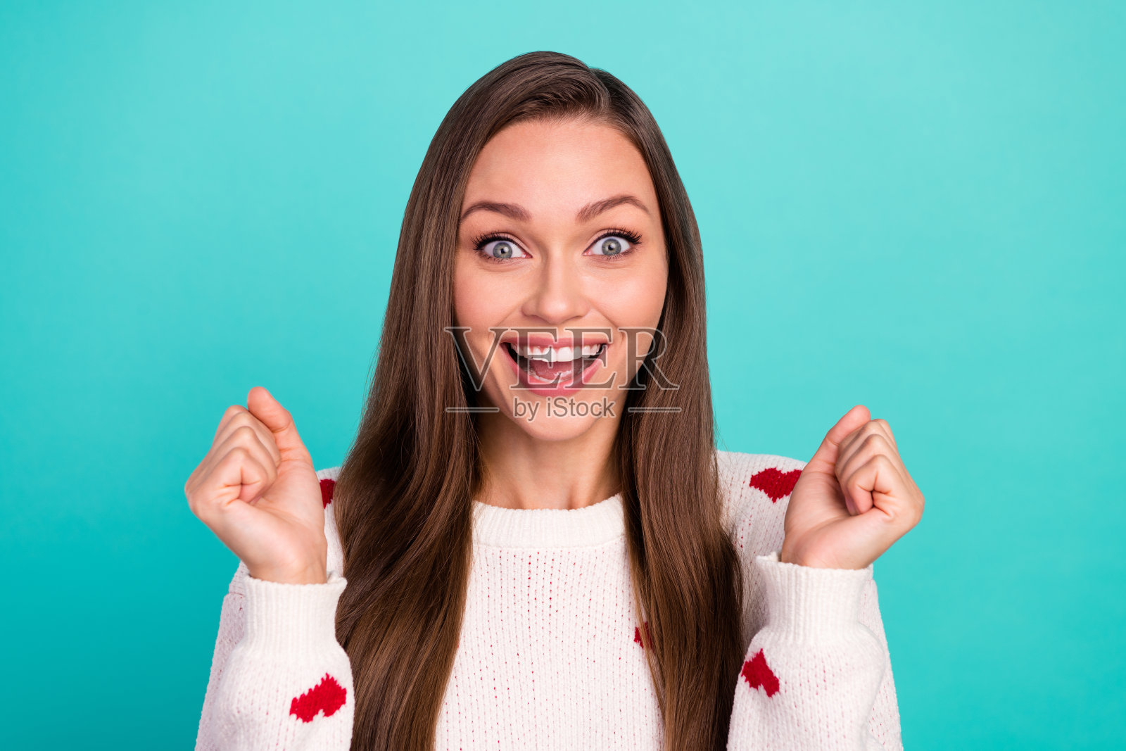 穿着白色套头衫的幸运女孩笑着举起拳头，隔离在蓝绿色背景上的照片照片摄影图片